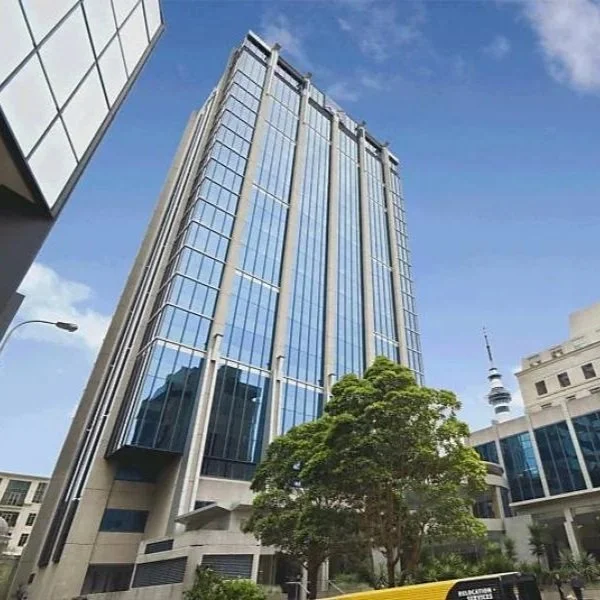 Tall modern glass office building with reflections, a tree in front, and a blue sky with some clouds.