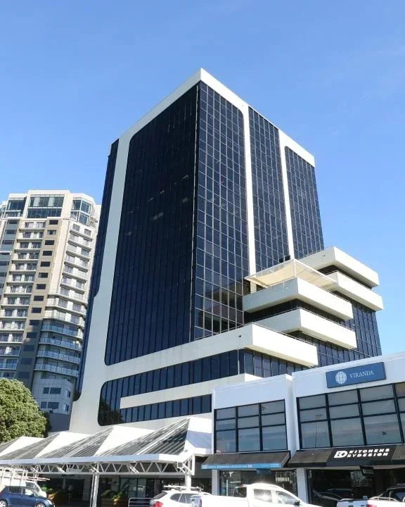 Modern high-rise office building with glass windows and white balcony structures against blue sky.
