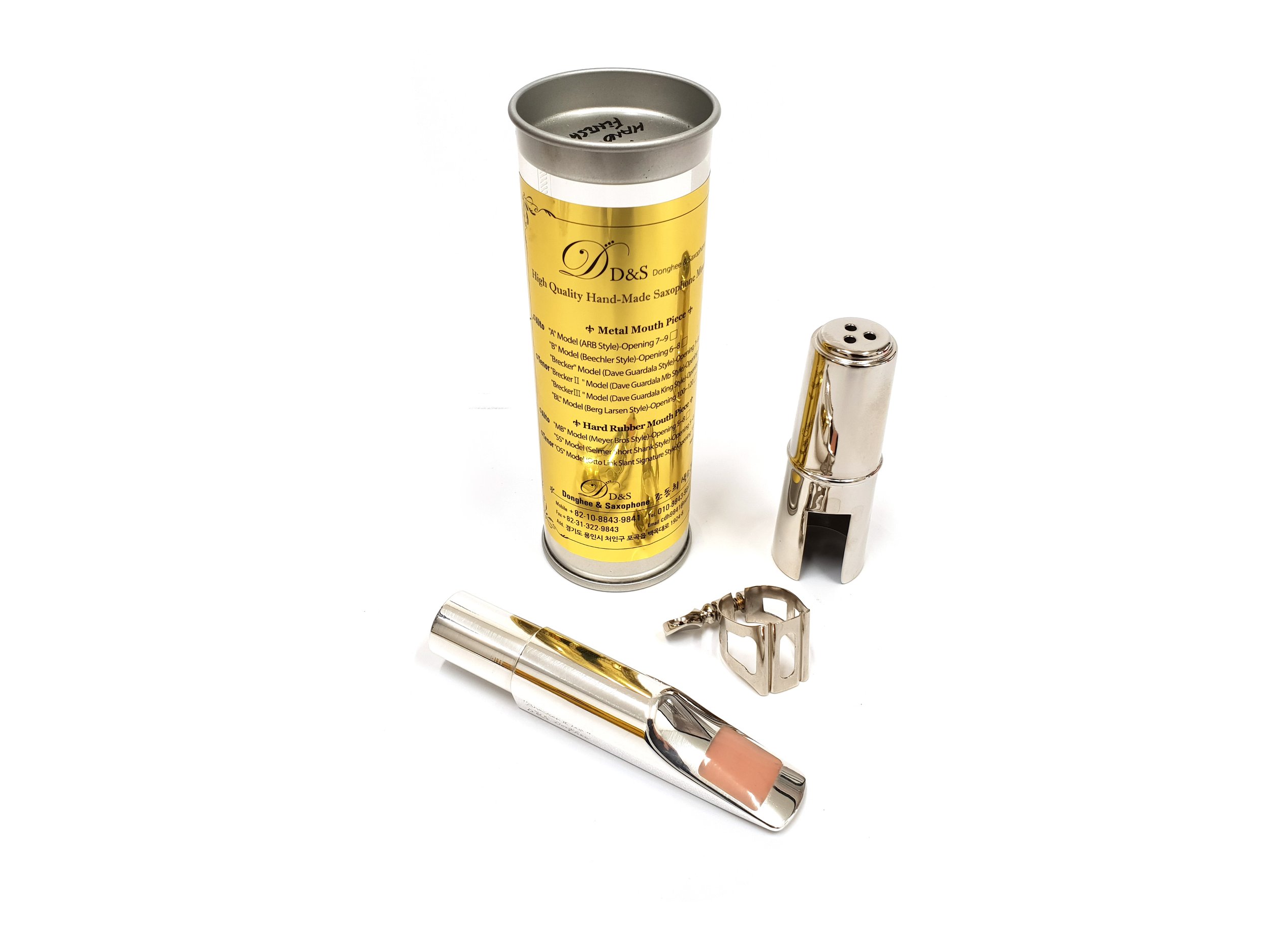 Metal saxophone mouthpiece set with ligature, cap, and yellow packaging tube on a white background.