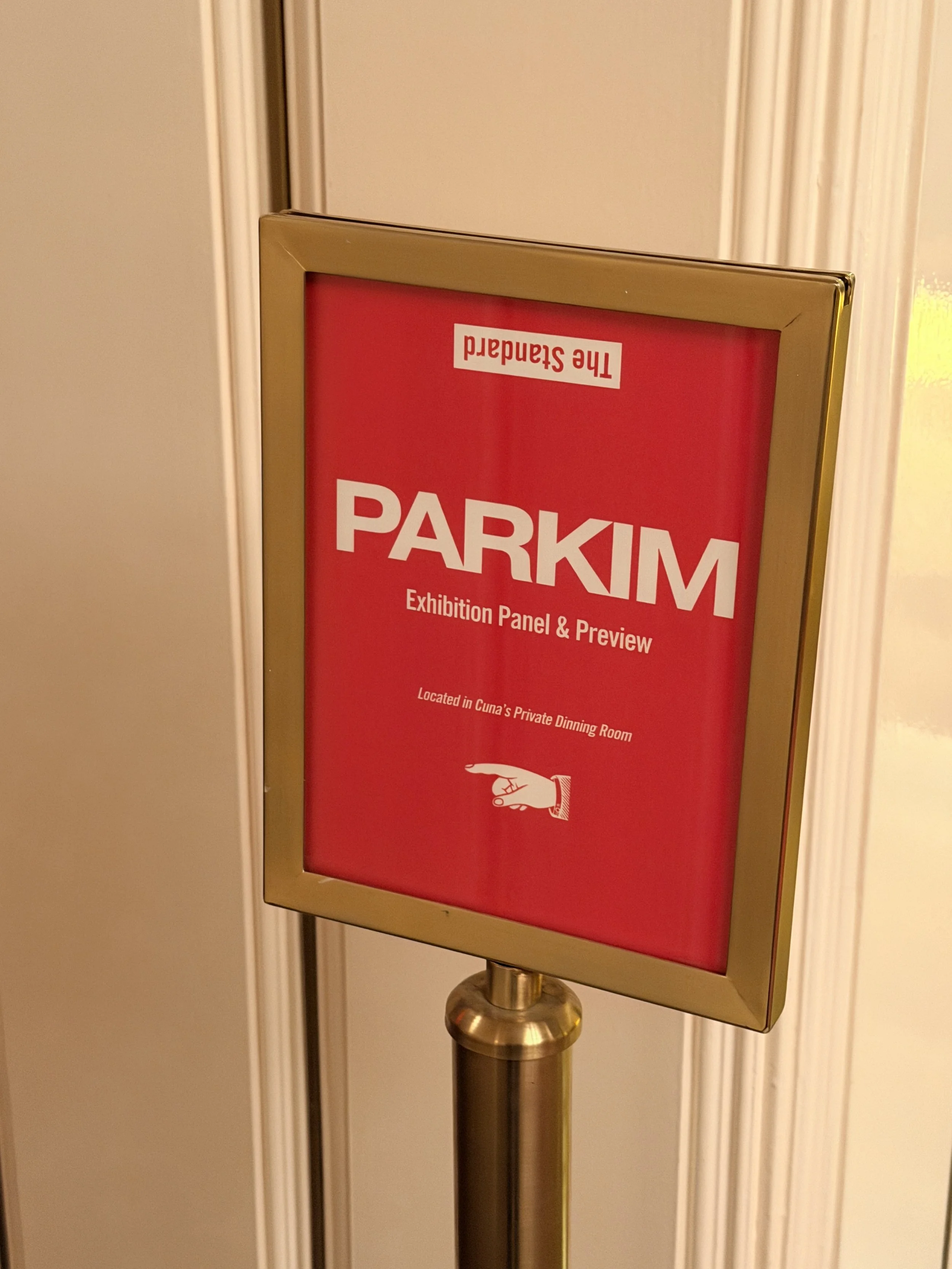 Red exhibition panel with the word 'PARKIM' and a pointing hand icon, mounted in a frame on a gold stand.