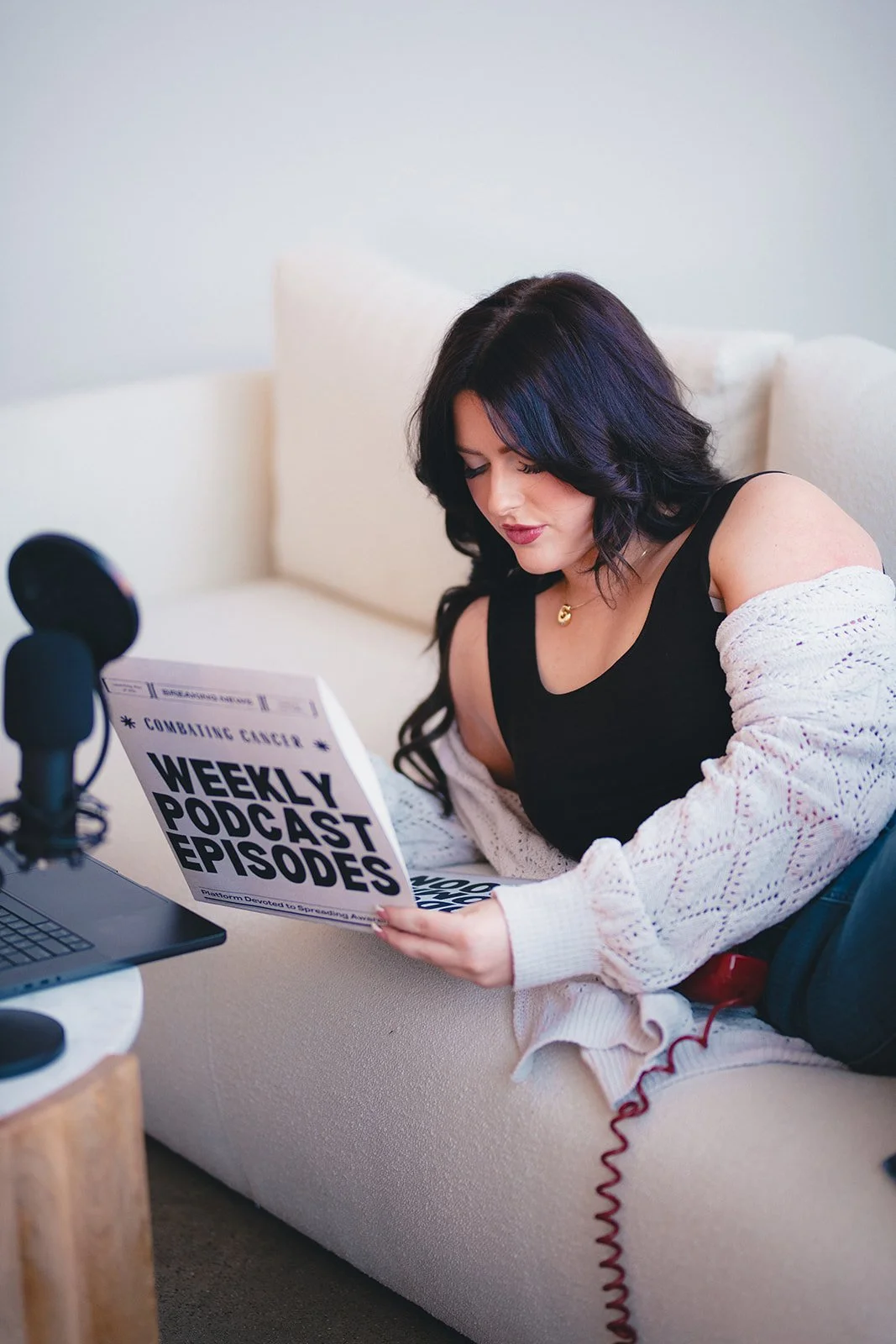 Woman reading a sign that says 'Weekly Podcast Episodes' in a cozy room with a microphone and laptop nearby.