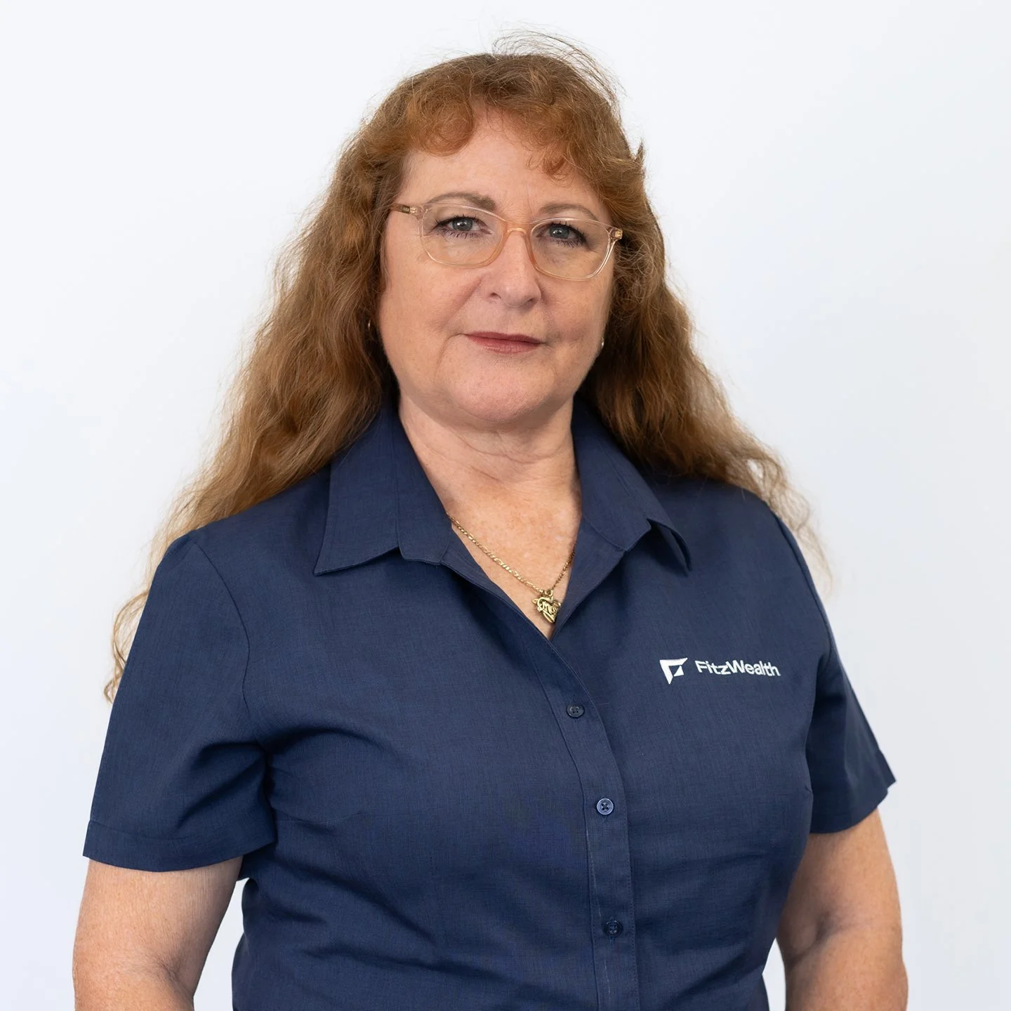 A woman with long curly blonde hair smiling at the camera, wearing a dark blue collared shirt against a light gray background.