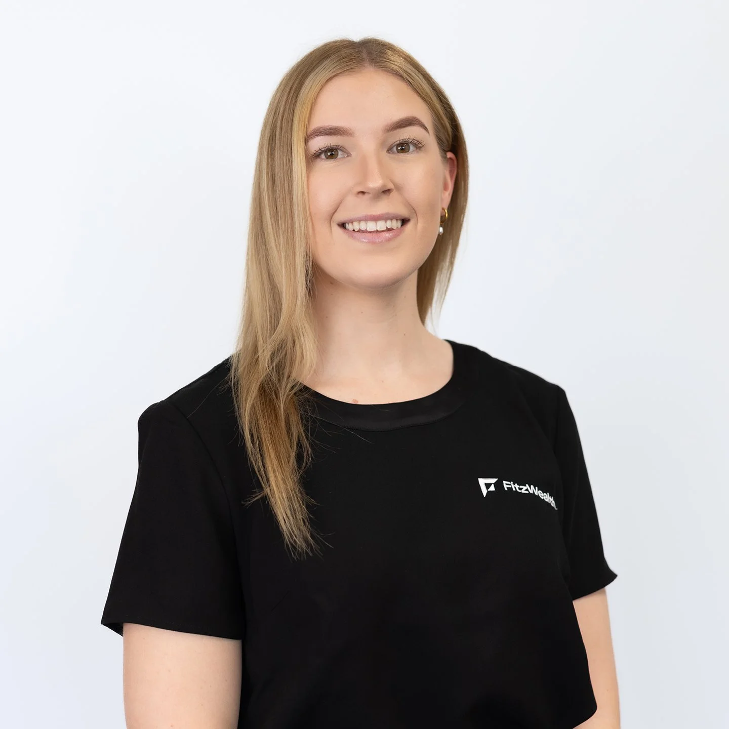 A young woman with long blonde hair wearing a black Fitnesswear t-shirt, smiling against a plain white background.