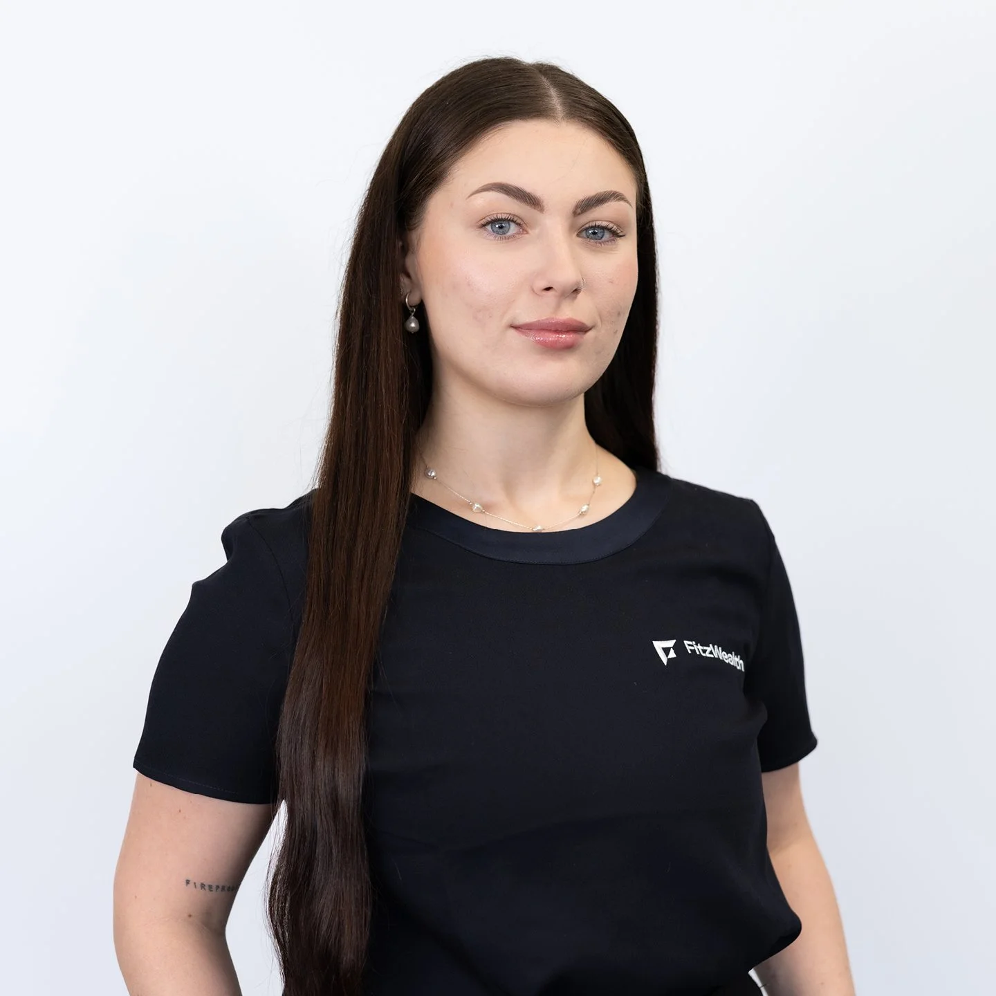 Young woman with long dark hair, wearing a black FitZNealyn T-shirt, posing against a plain white background.