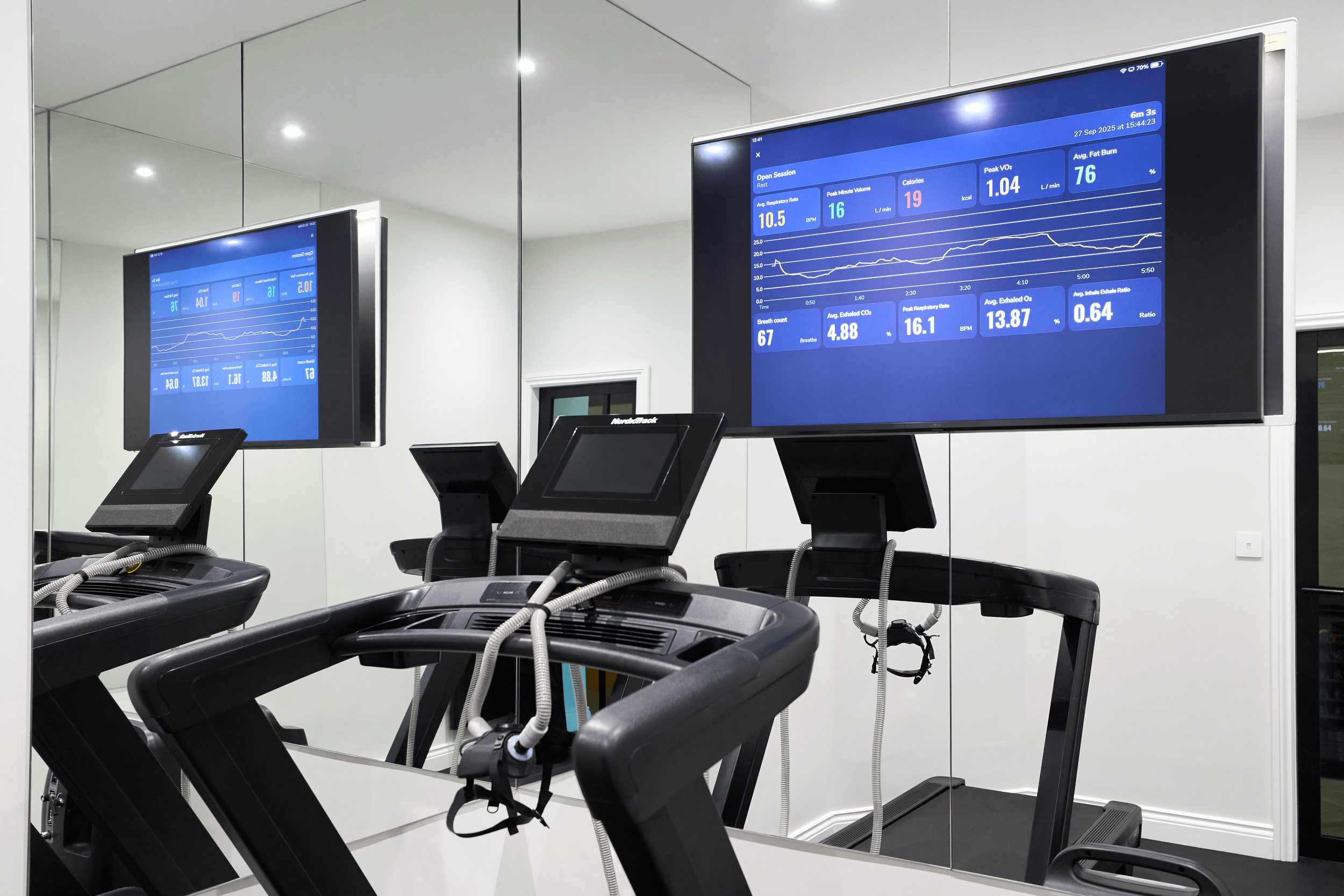 A man is altitude training on a stationary bike while wearing a breathing mask during a clinical test at the EWOT (Exercise With Oxygen Therapy) center, with the sign 'EWOT The Outpost' visible on the wall behind him.