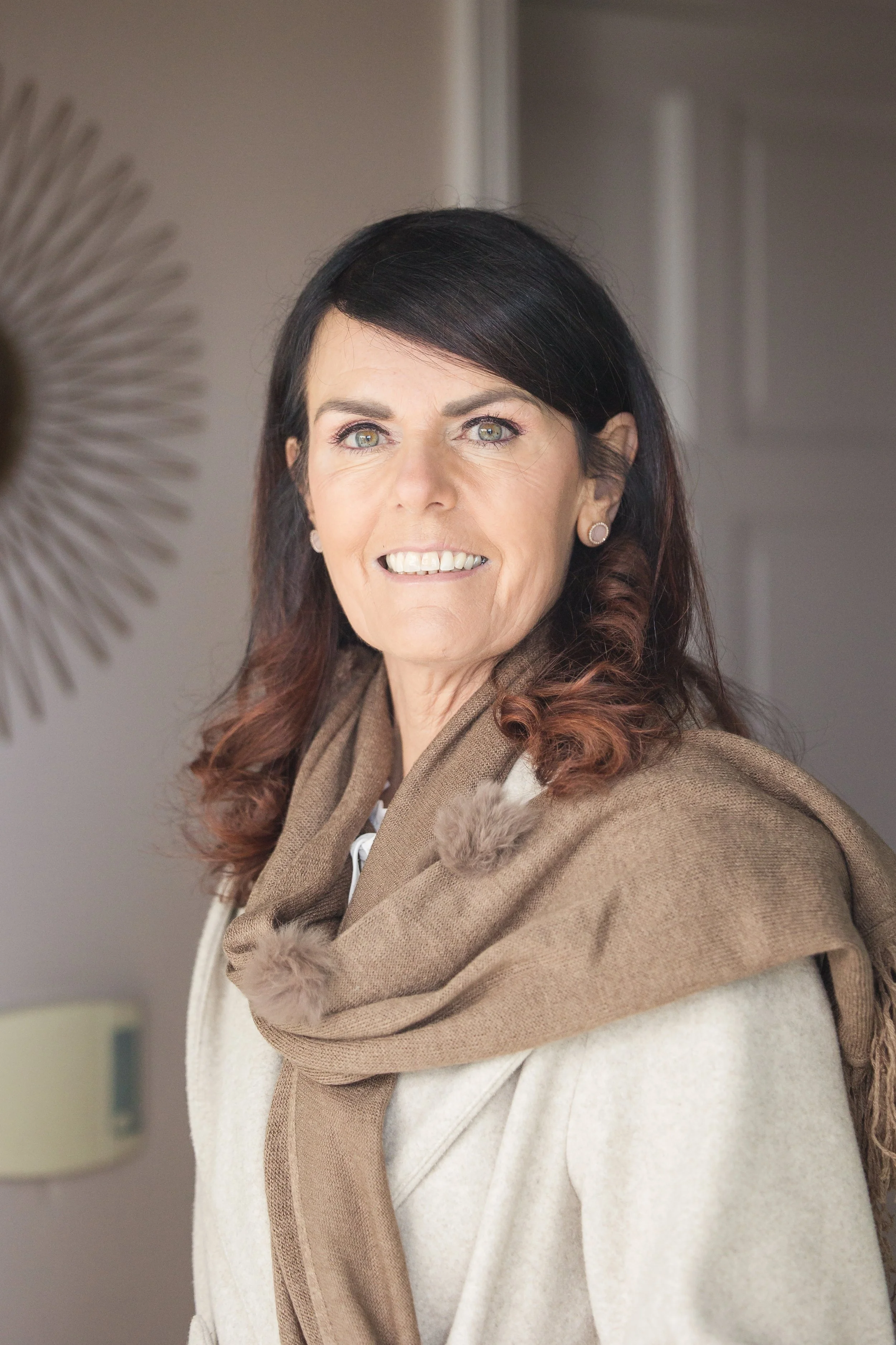 Woman with dark hair and a brown scarf smiling indoors
