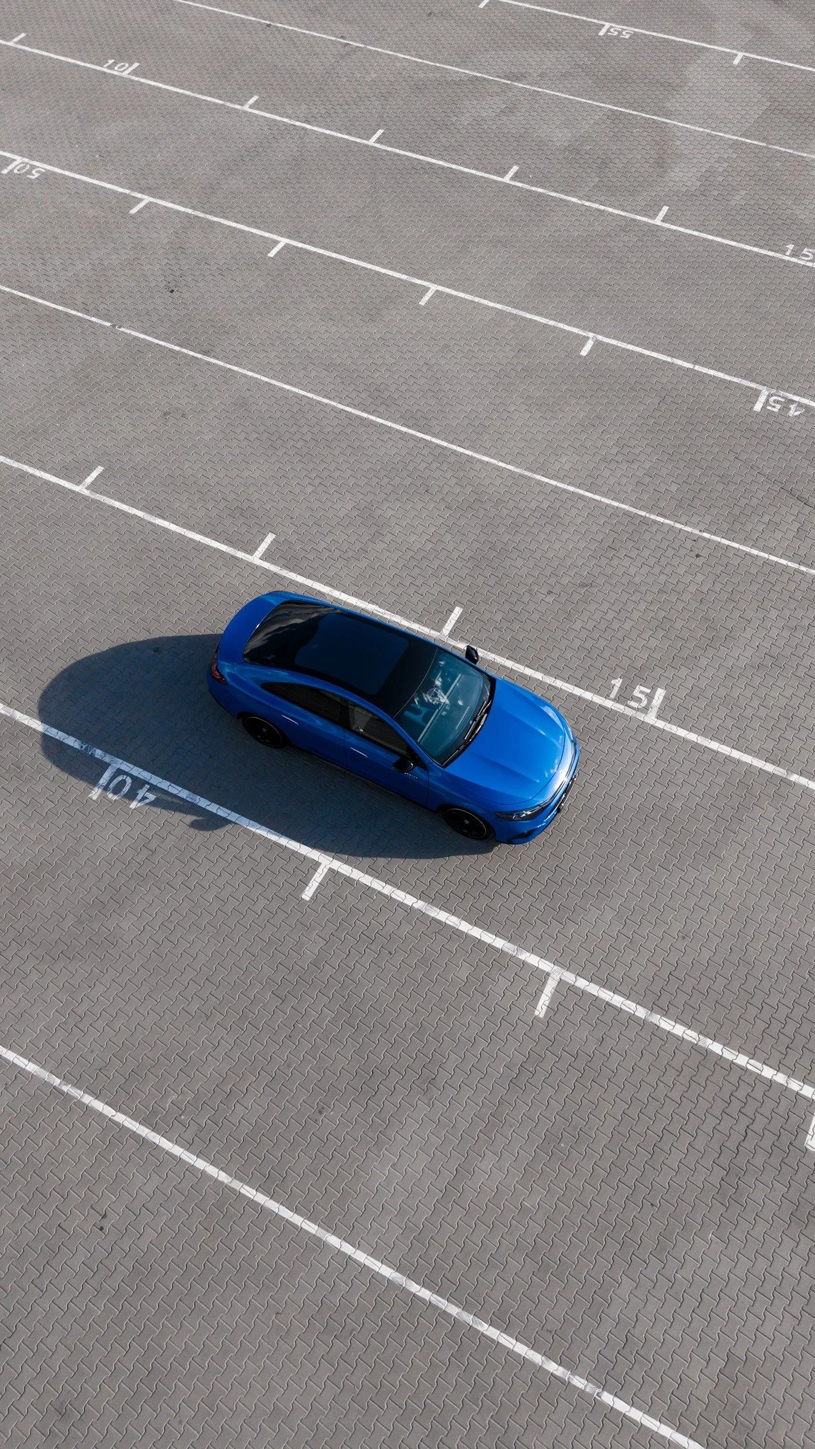 A blue car parked in an empty outdoor parking lot with marked spaces, no other vehicles or people present.