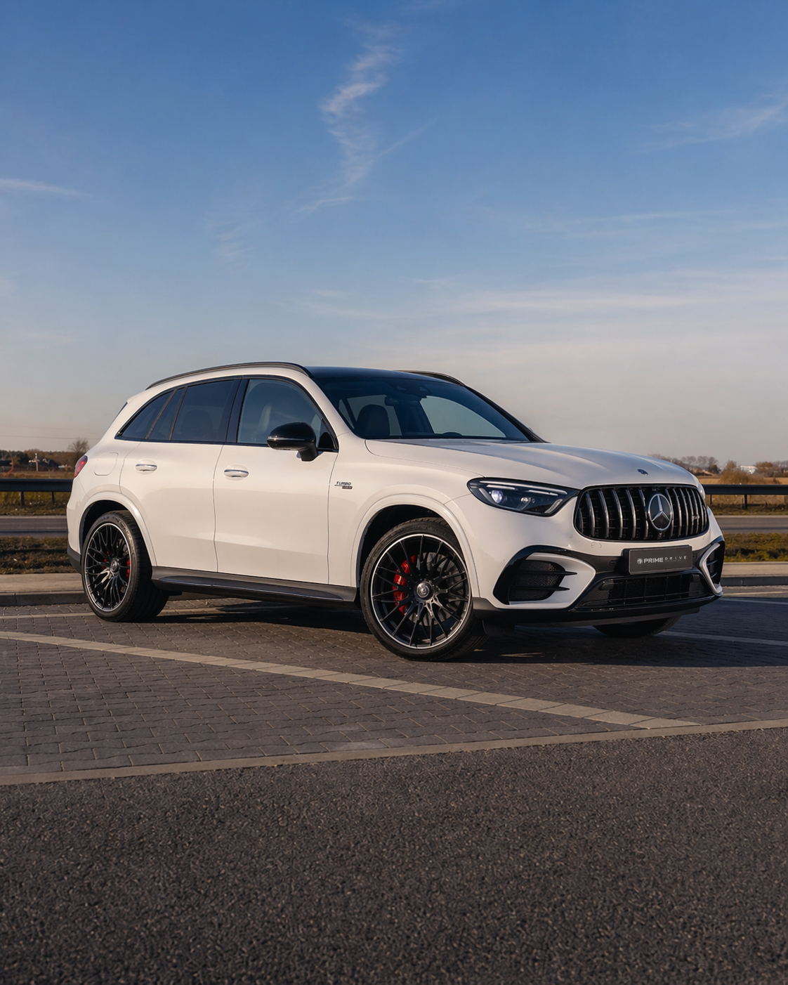 White Mercedes-Benz SUV parked on a paved area near a highway, under a clear blue sky.