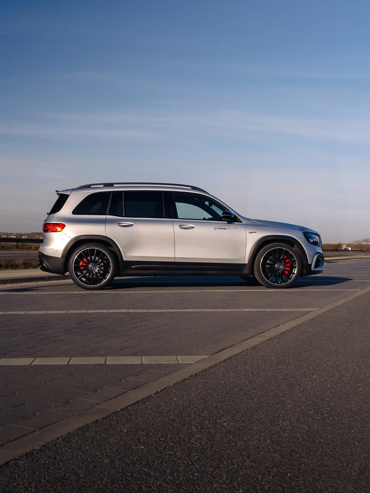 A silver Mercedes-Benz SUV parked on the side of a road with clear blue sky in the background.