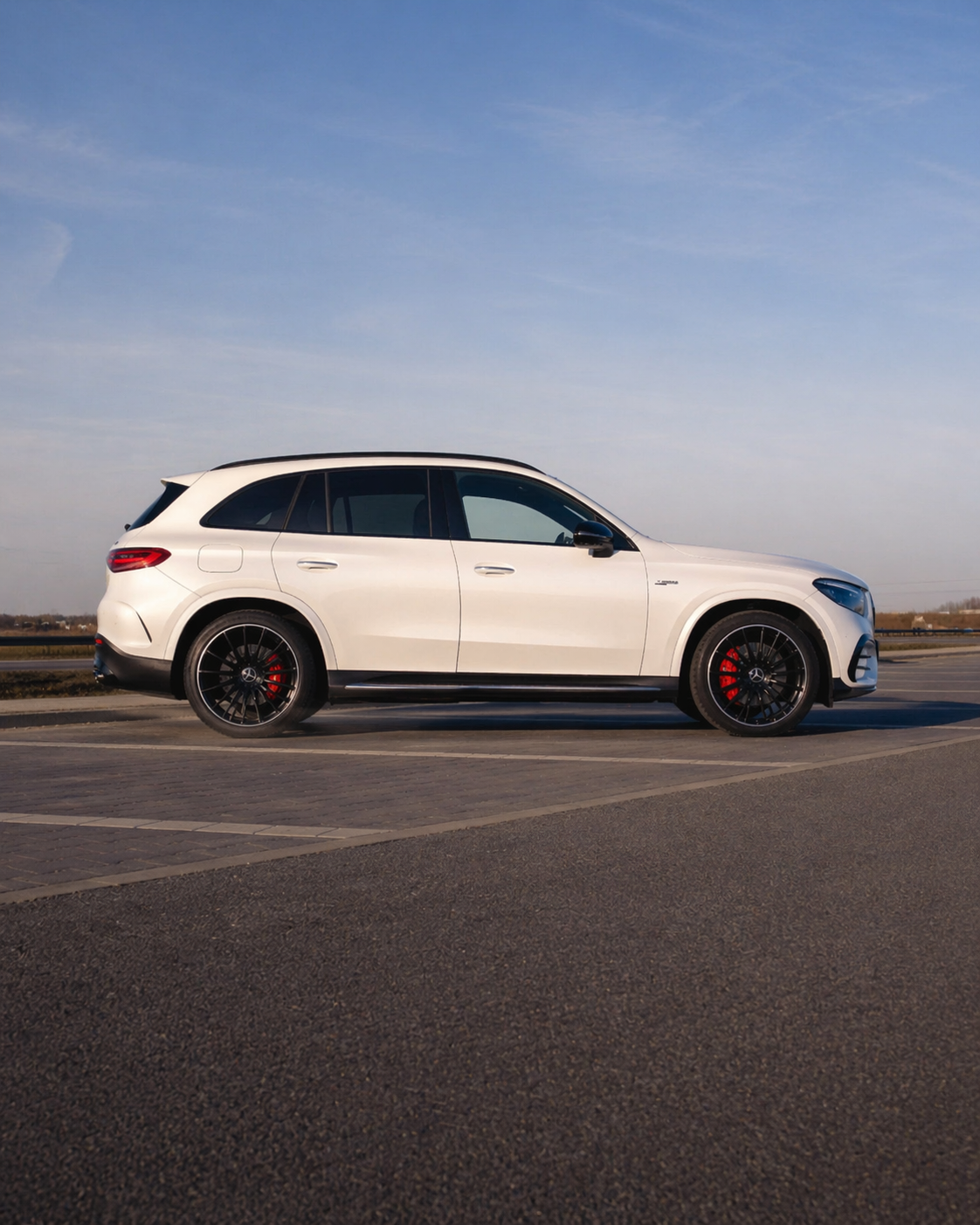 White luxury SUV parked on the side of a road under a clear blue sky.