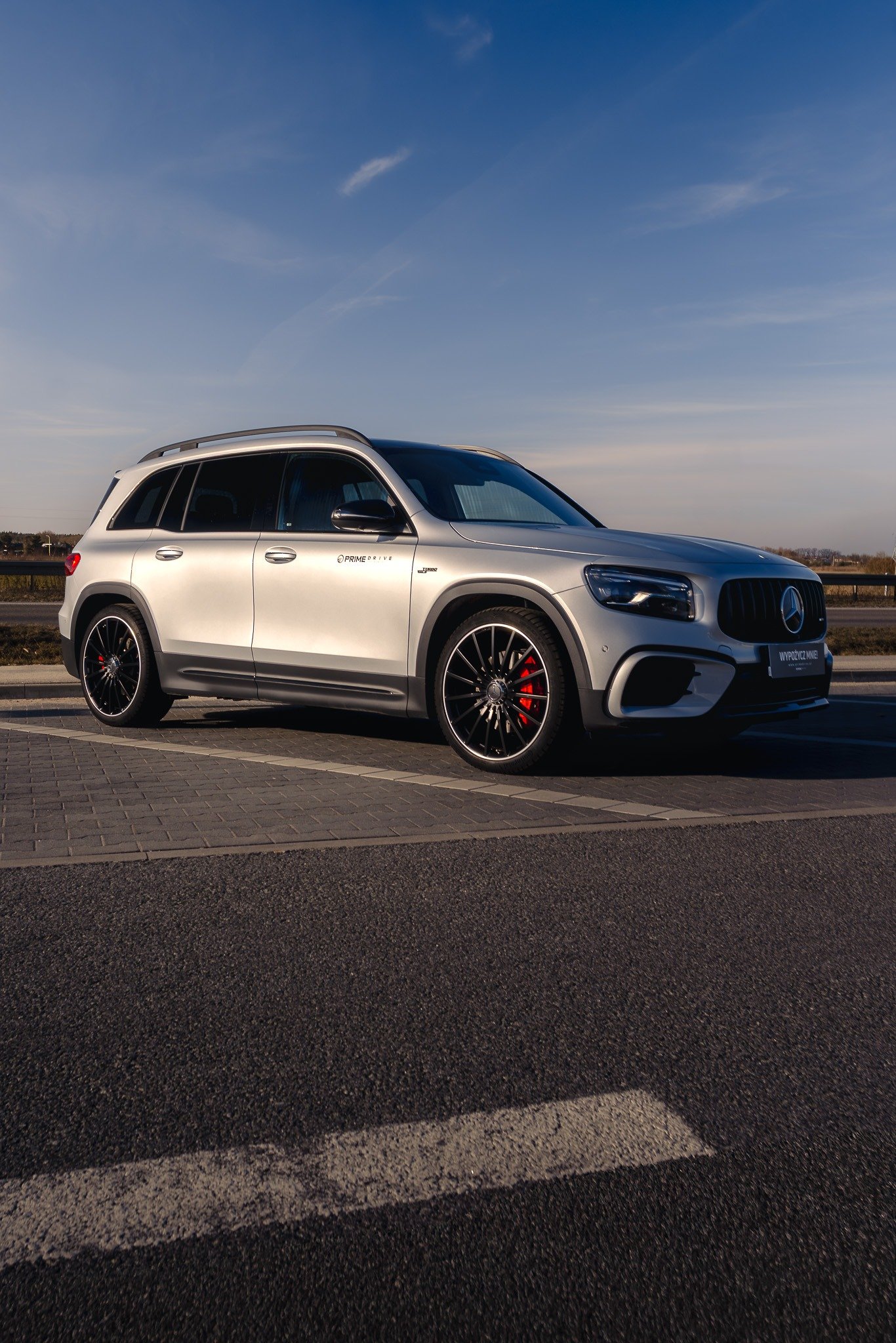 A white Mercedes-Benz SUV parked on the side of a road under a clear blue sky with a few clouds.