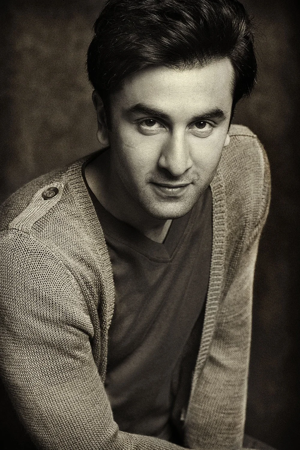 Black and white portrait of a young man with dark hair, wearing a sweater and a T-shirt, looking at the camera with a slight smile.