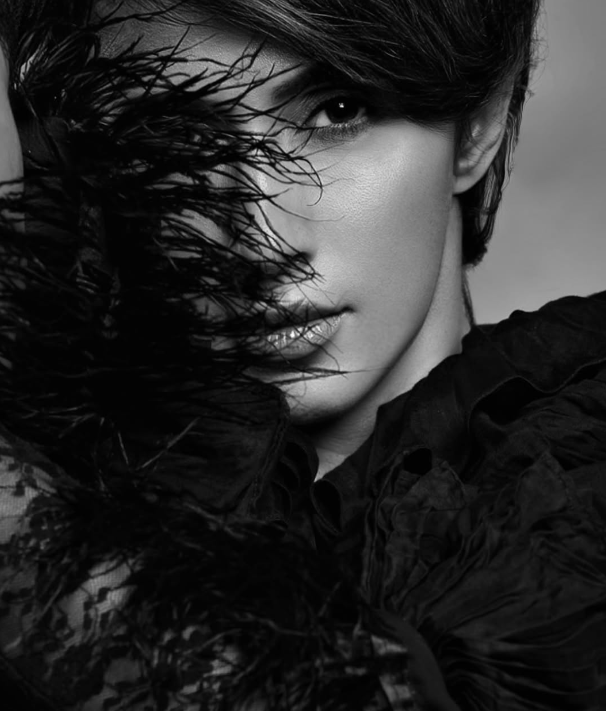 A black-and-white close-up portrait of a woman with wet hair partially covering her face, wearing a dark textured garment.