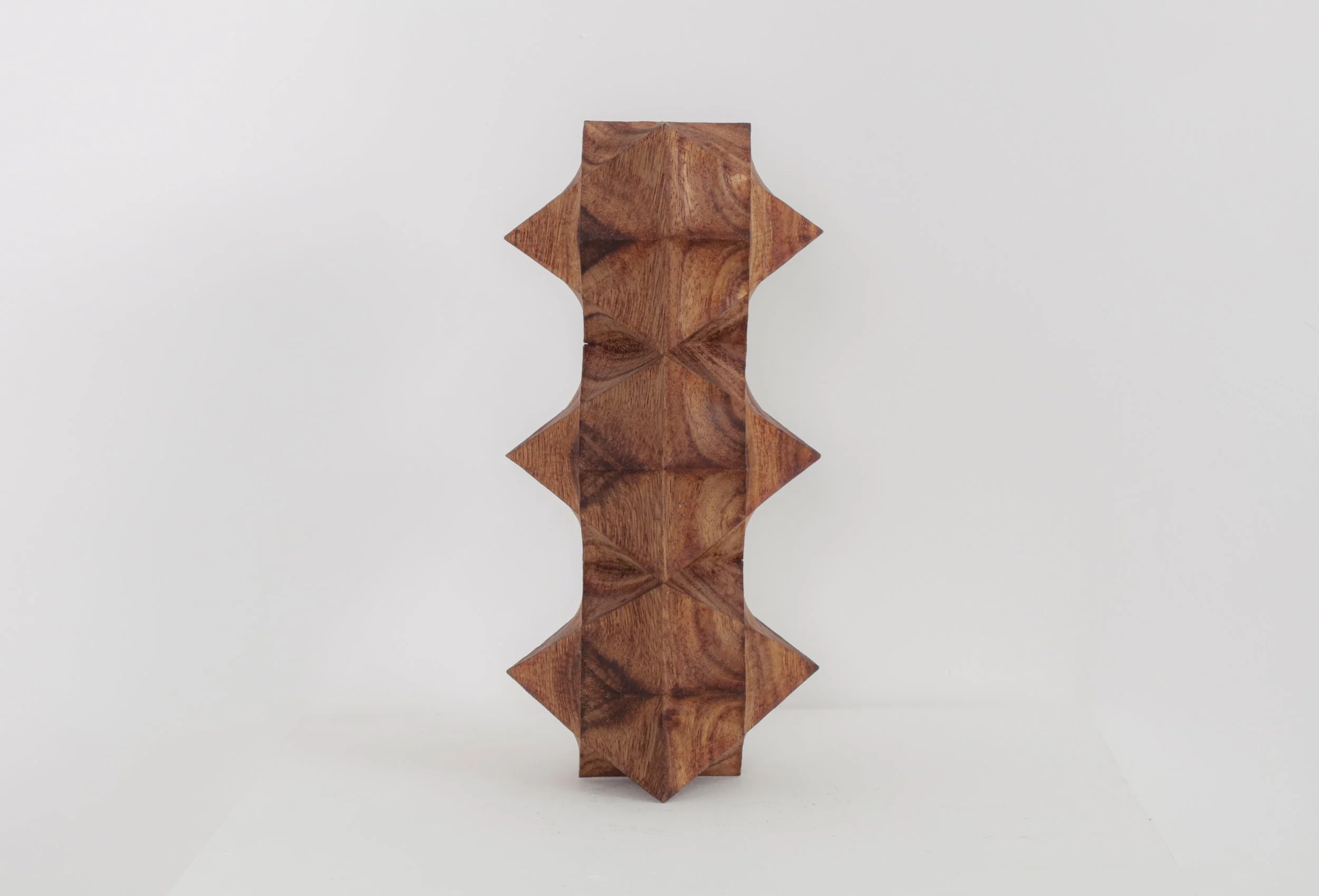Tall wooden sculpture with geometric, pyramid-like shapes and a natural wood finish, placed against a plain white background.