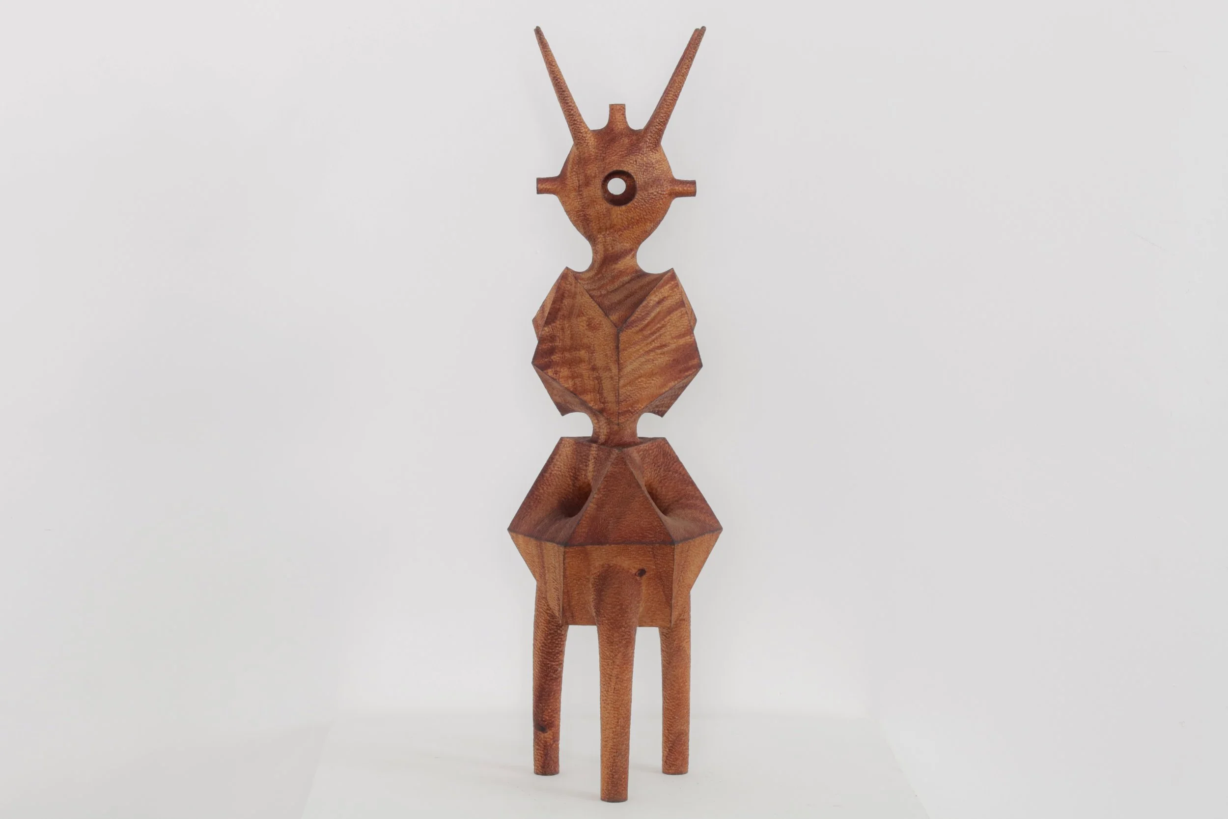 Wooden sculpture of a stylized ant with geometric shapes and elongated antennae, set against a plain white background.