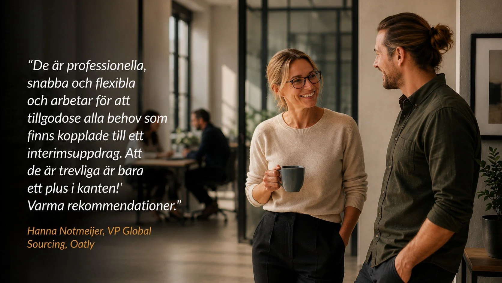 Två personer som står och pratar, en kvinna med glasögon och en man med uppsatt hår, i ett kontorsmiljö. Kvinnan håller en kopp.