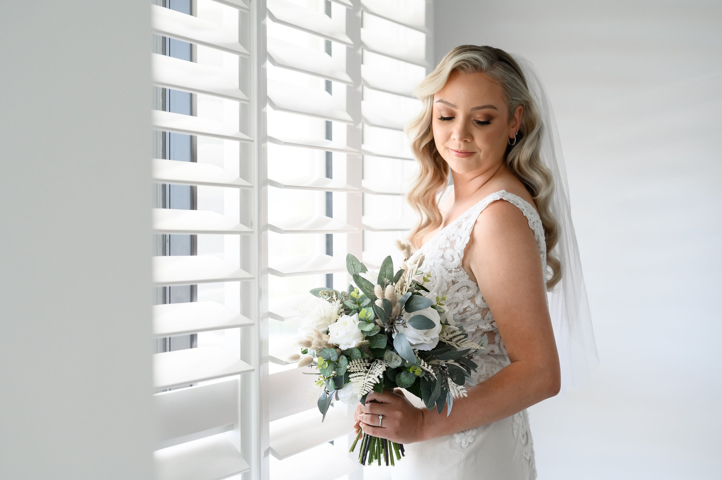 Bride in lace wedding dress holding bouquet by window