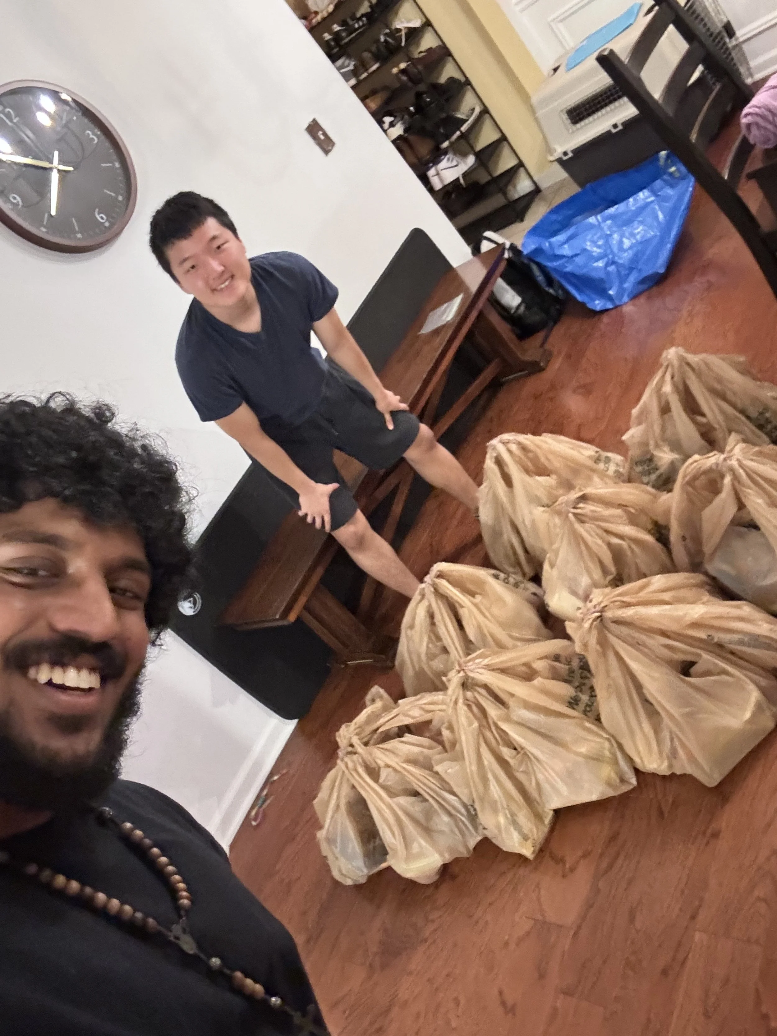 Two smiling men standing in a room with bags of groceries laid out on the floor.