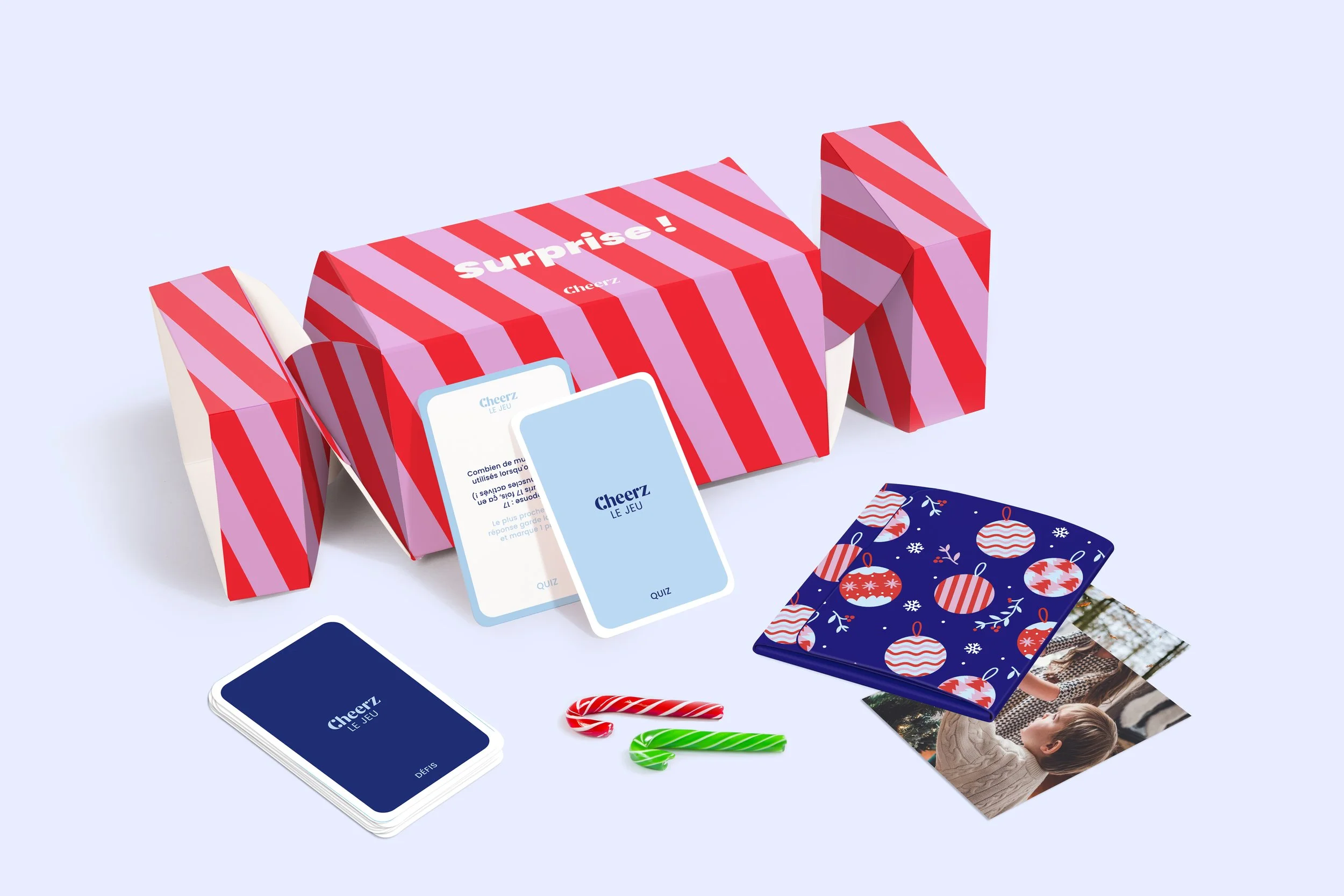 Jeu de société avec cartes, bonbons, photos, et boîte à motifs rouges et roses sur fond blanc.