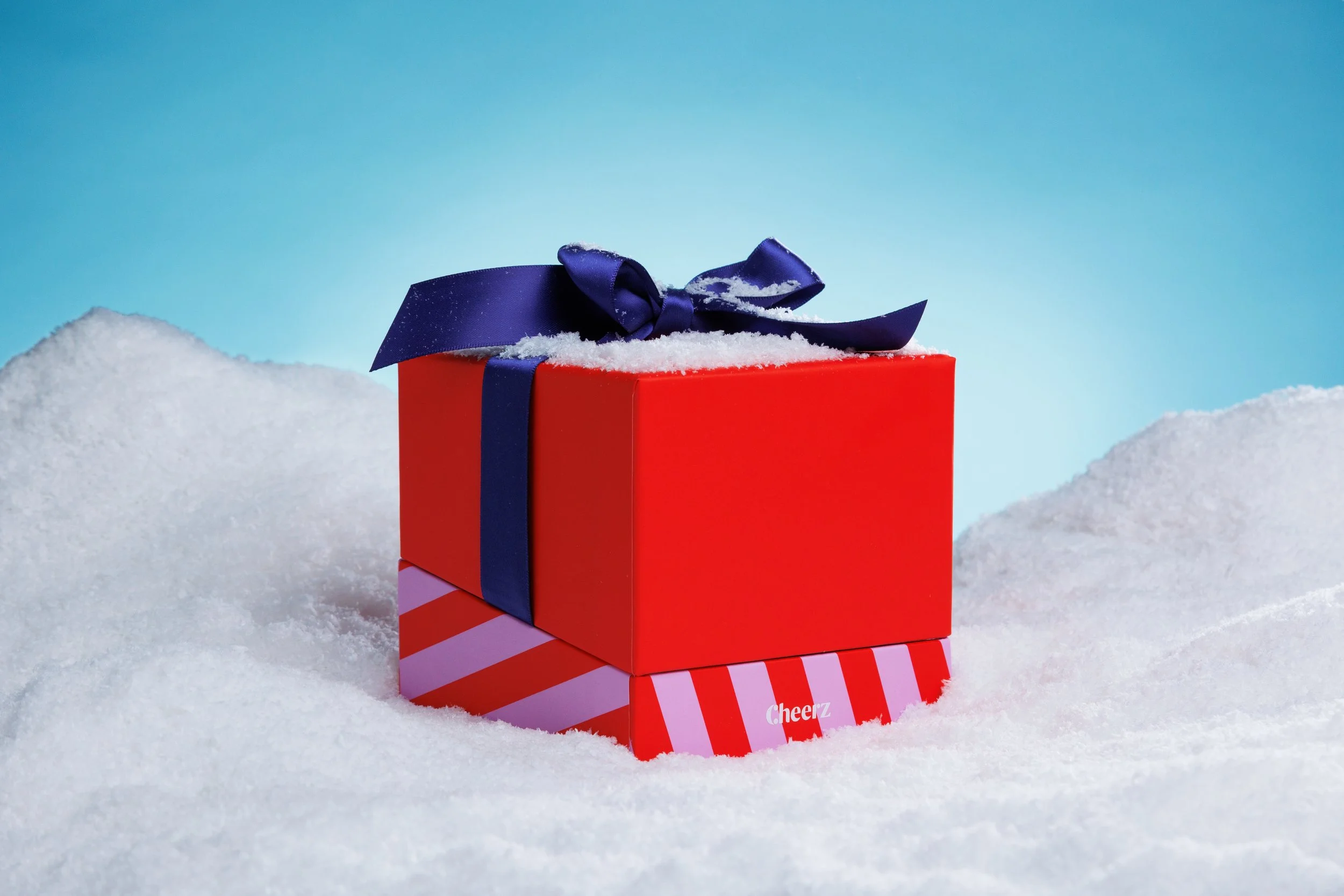 Coffret cadeau rouge avec ruban violette dans la neige, sous un ciel bleu.