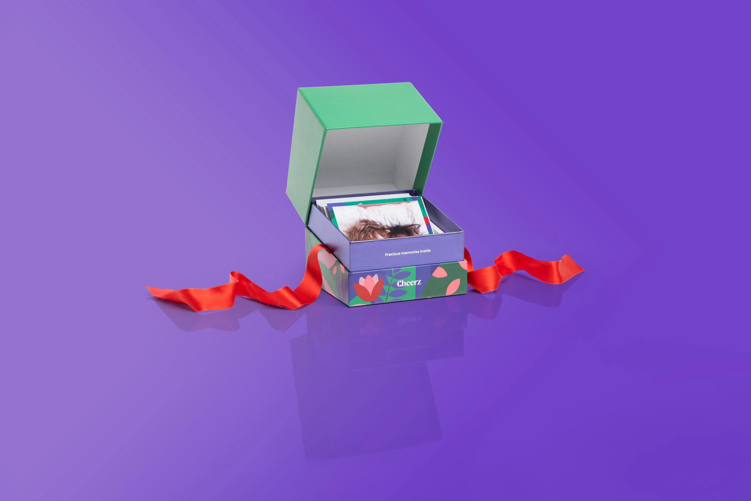 Une boîte cadeau colorée avec une photo d'une personne à l'intérieur, entourée d'un ruban rouge, sur un fond violet.