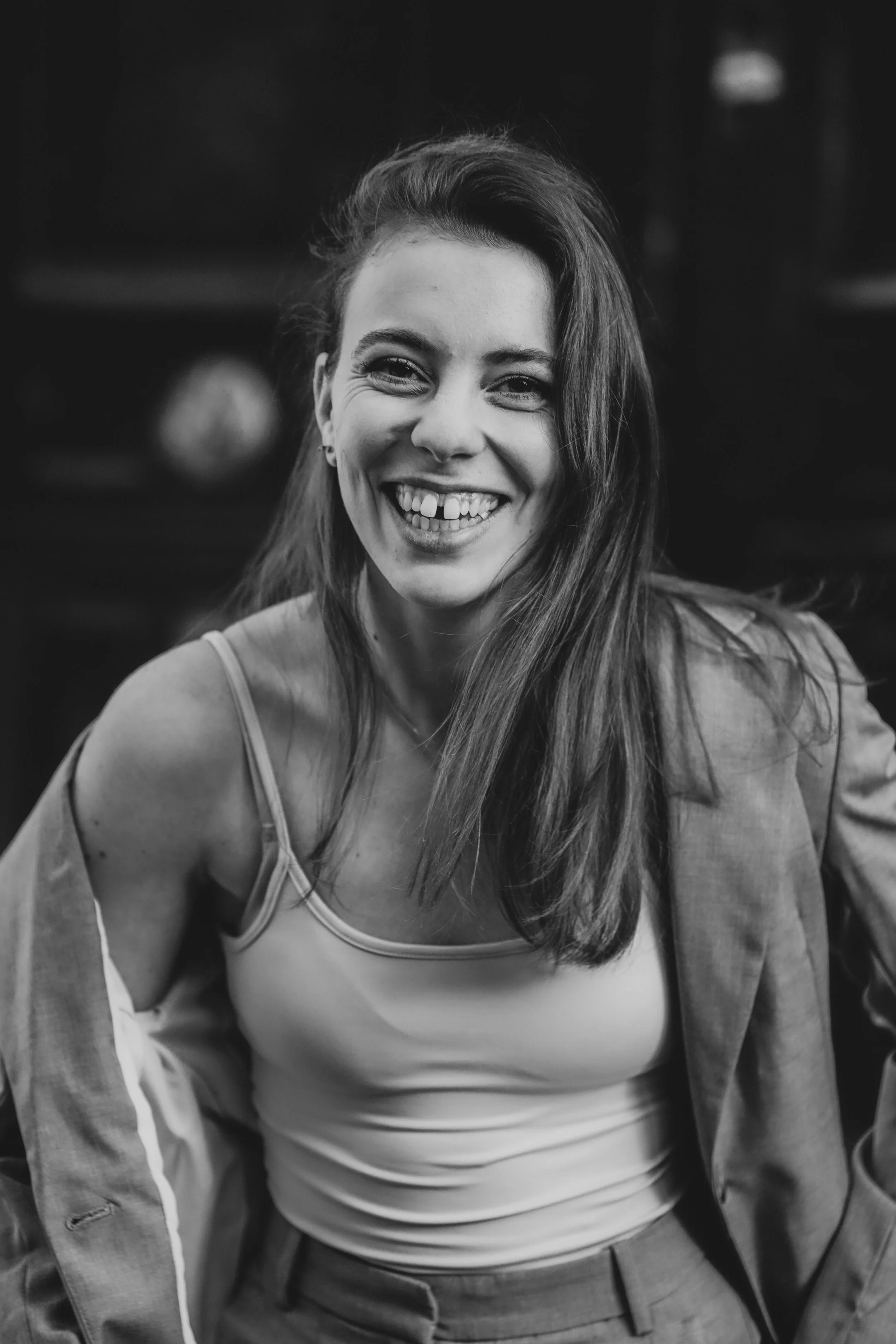 Une femme souriante avec des cheveux longs, portant un sweat et un pantalon, en noir et blanc.