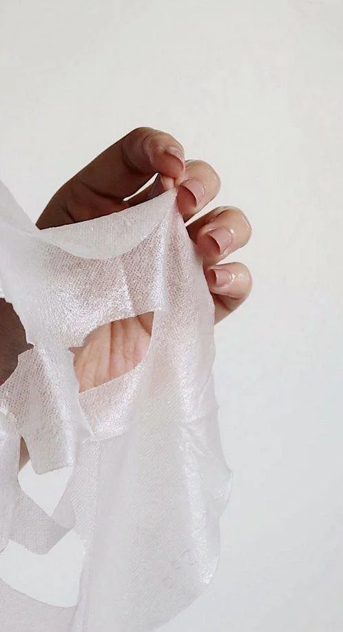Close-up of a hand peeling a sheet face mask off skin.