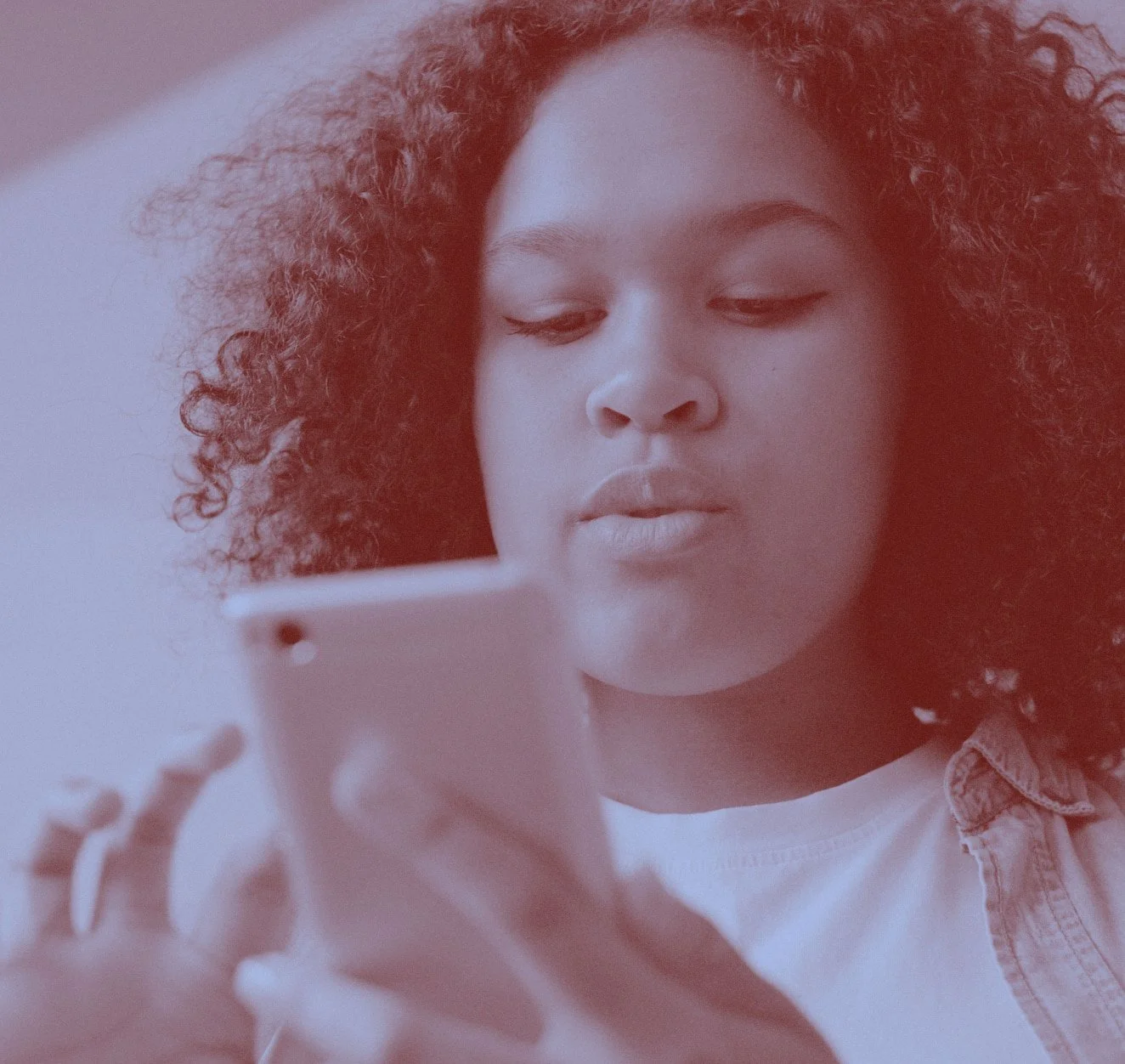 A young woman looking down at a phone she is holding. Duotone blue and grain effect applied.