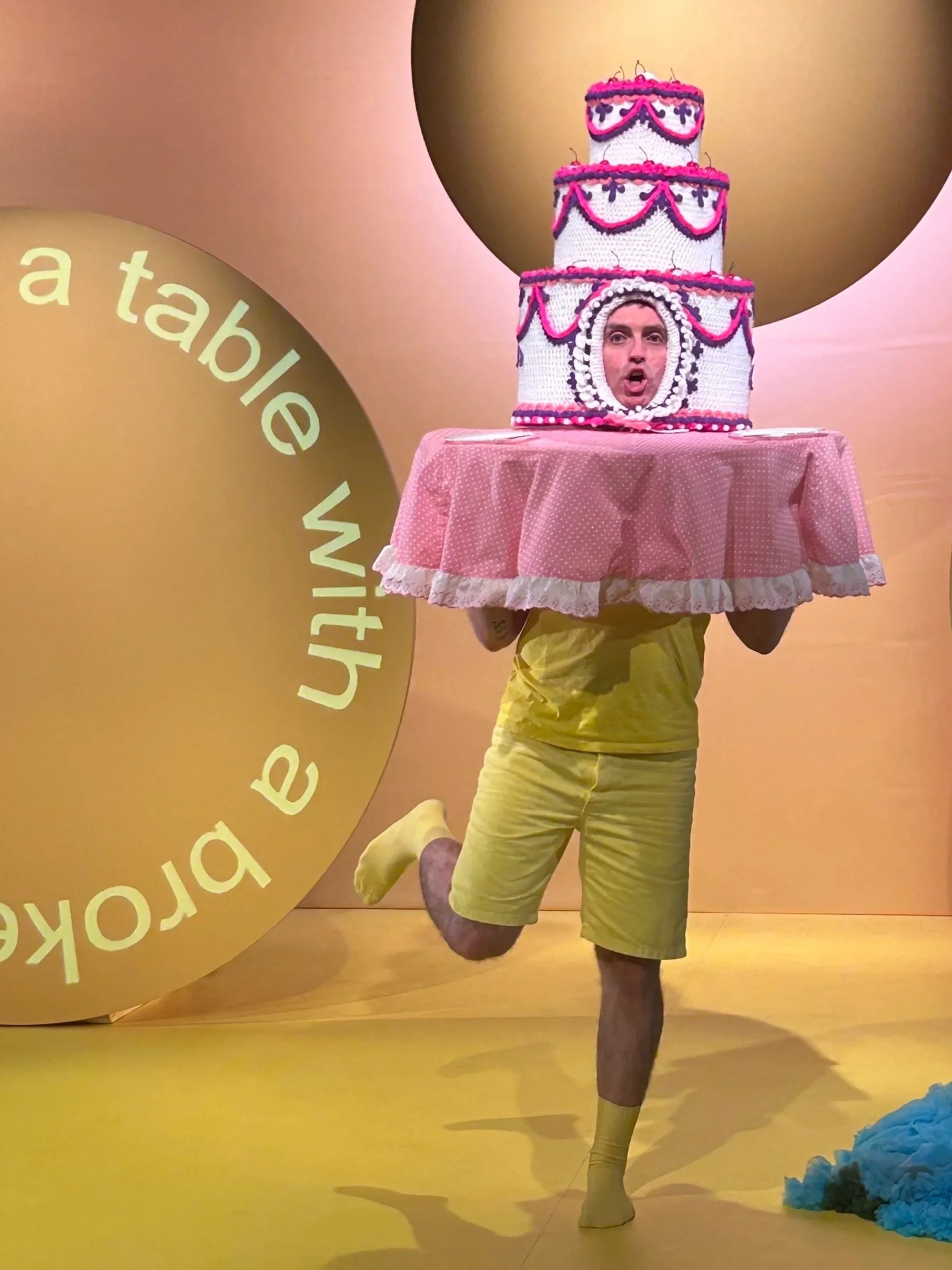 Man on a yellow stage set wearing a cake hat.