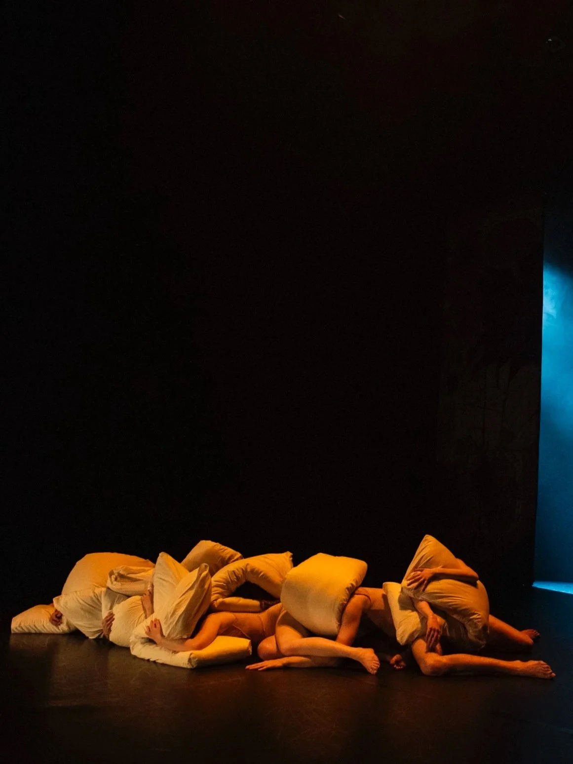 Dancers in a heap with large pillows.