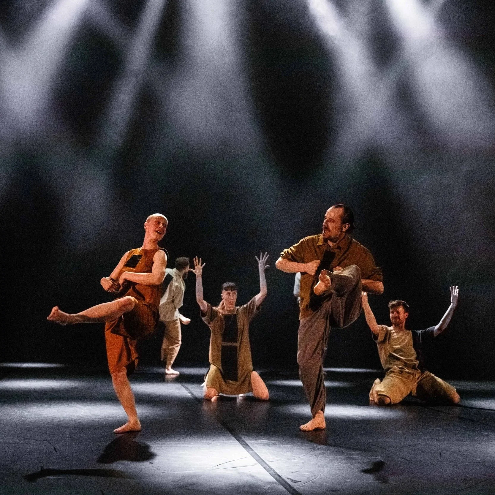 Dancers performing quirky geometric movements on a black stage.