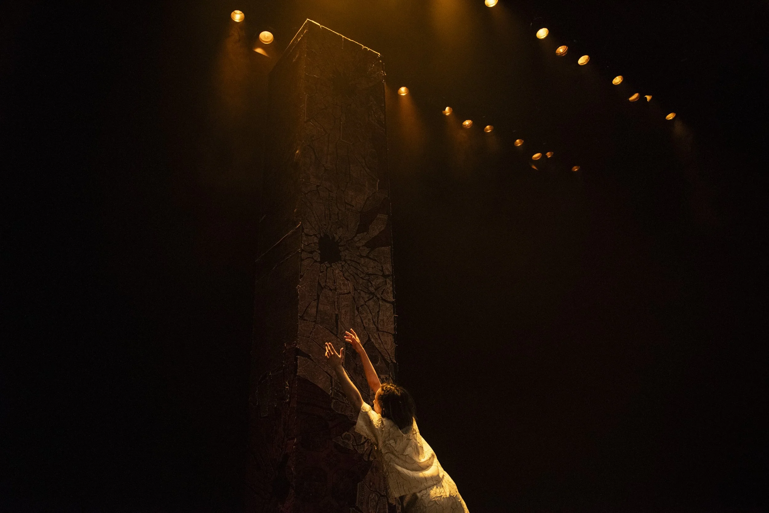 dancer stretches towards a tall monolith.