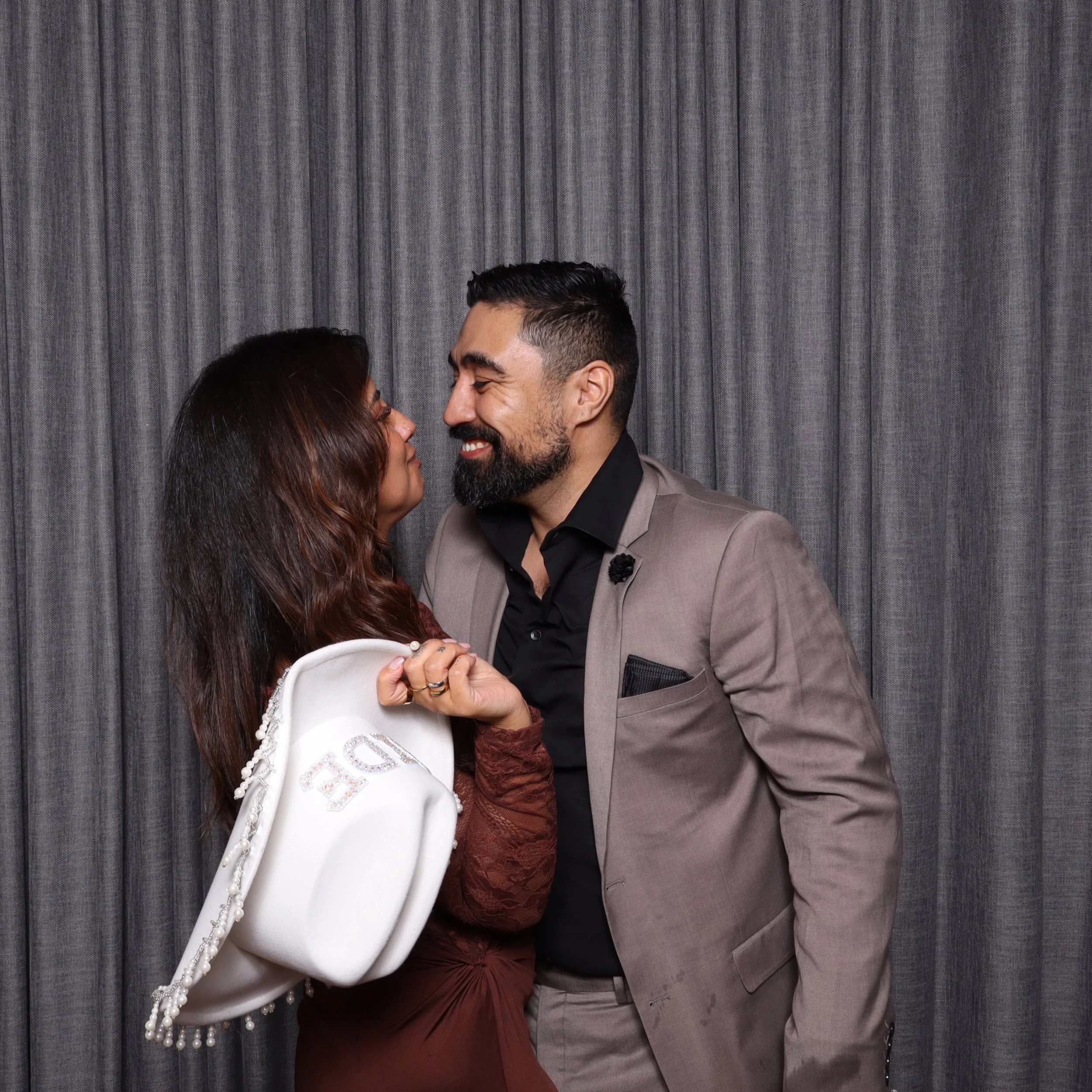 A man and woman face each other close, smiling, against a gray curtain backdrop.