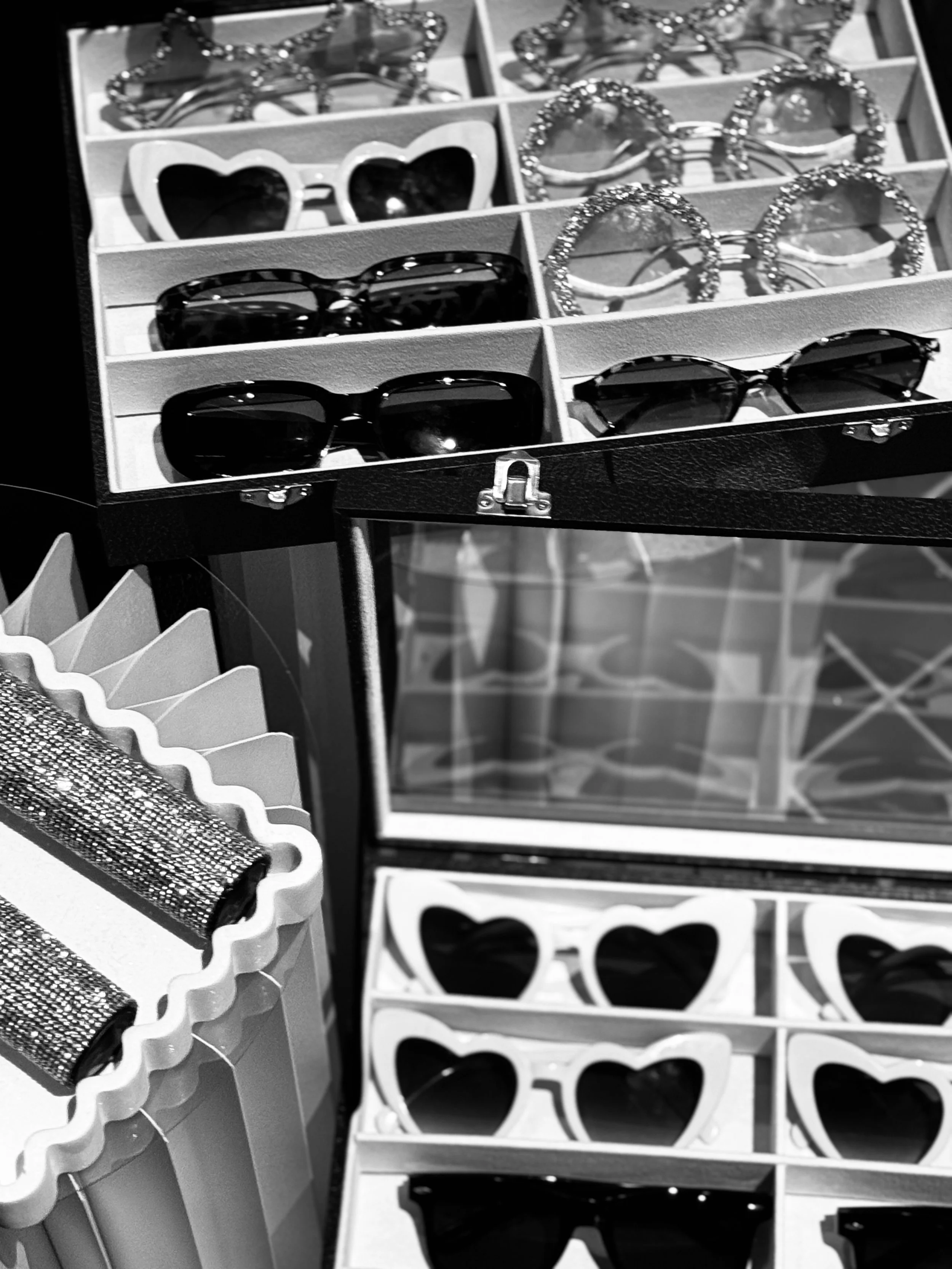 Display case with various sunglasses, including heart-shaped and rhinestone designs, on a plinth.