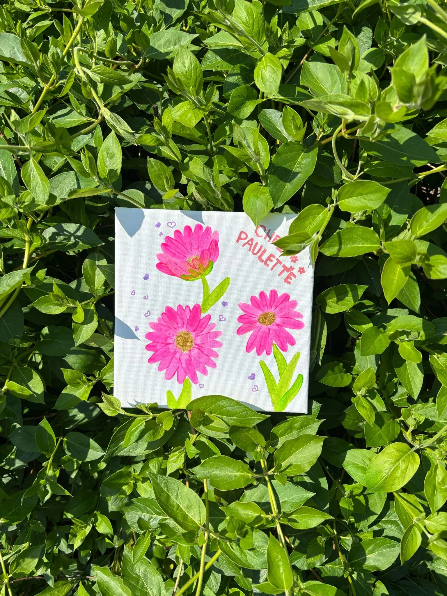 Petite toile peinte avec des fleurs roses sur un fond de feuilles vertes.