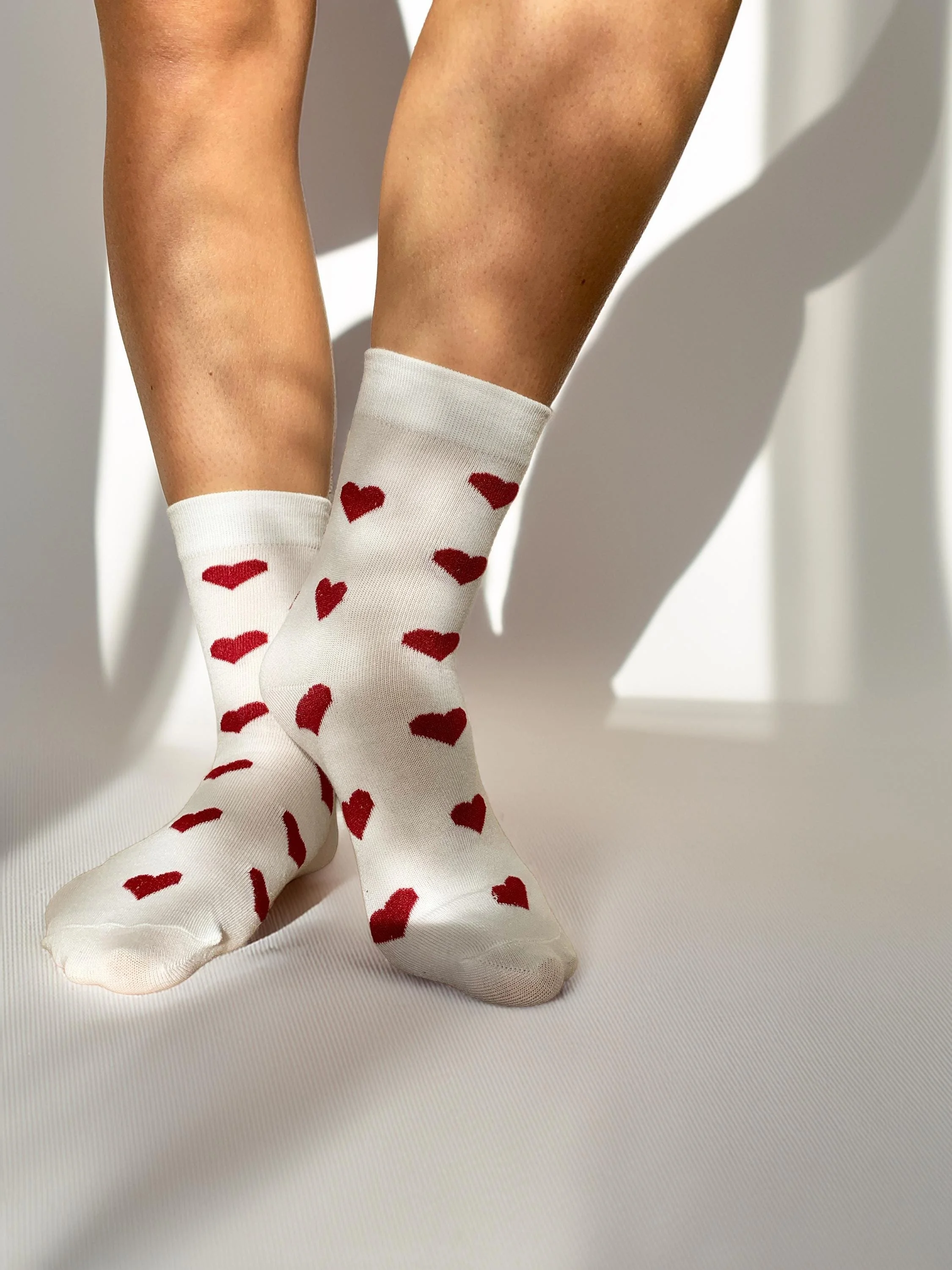 Beine mit weißen Socken mit roten Herzmustern gegen einen weißen Hintergrund.