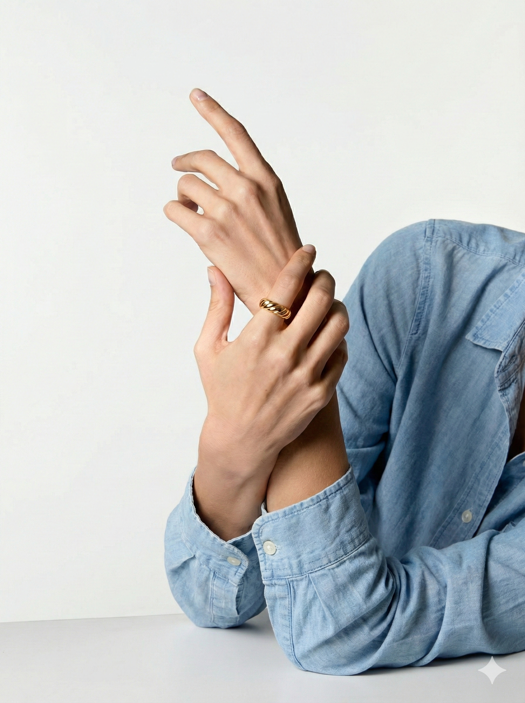 Nahaufnahme einer Person, die auf einem weißen Tisch sitzt, trägt eine goldene Ringschließe und bügelfreie hellblaue Jeansjacke, zeigt mit ihrer rechten Hand nach oben.