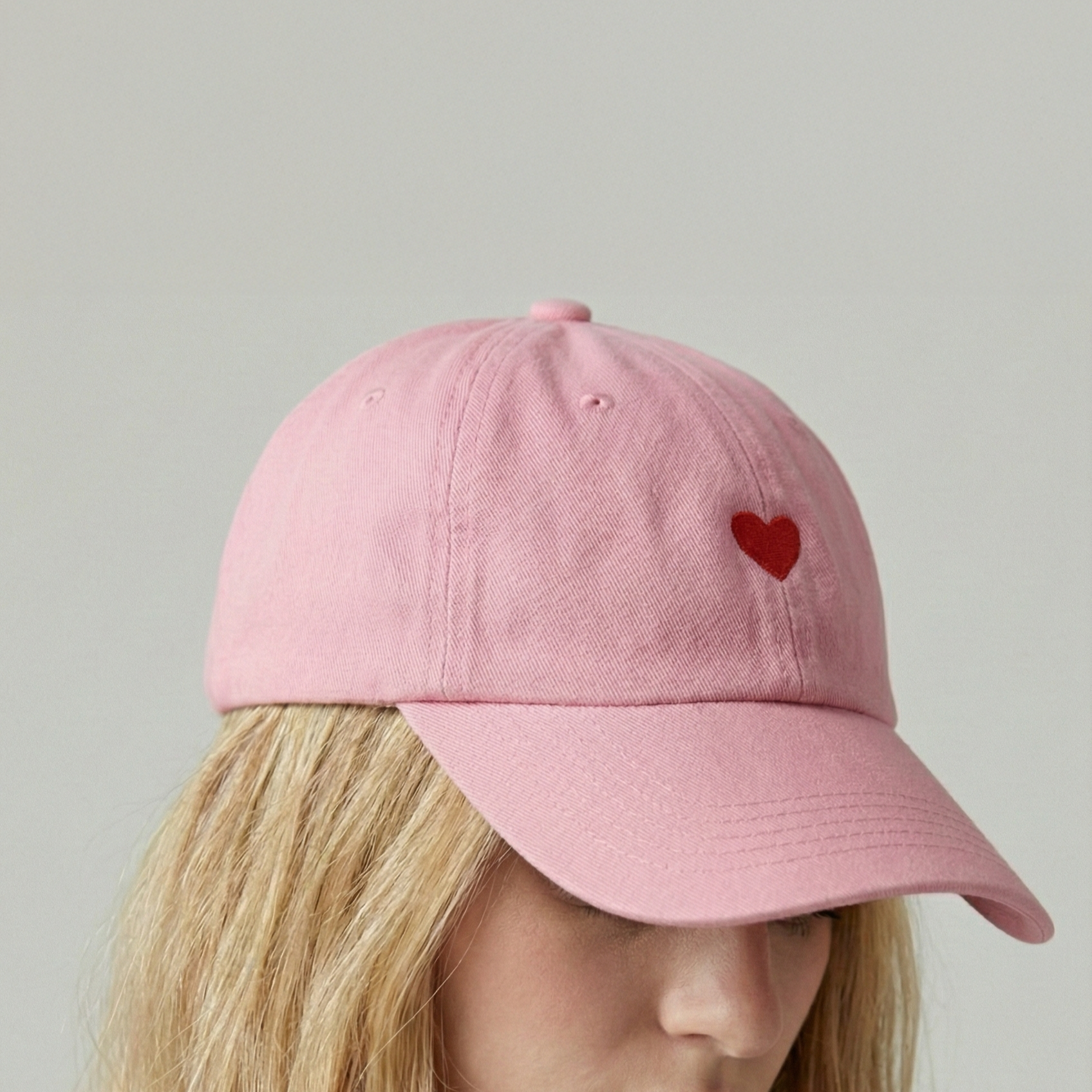 Eine Person trägt eine rosa Baseballkappe mit einem kleinen roten Herz auf der Seite.