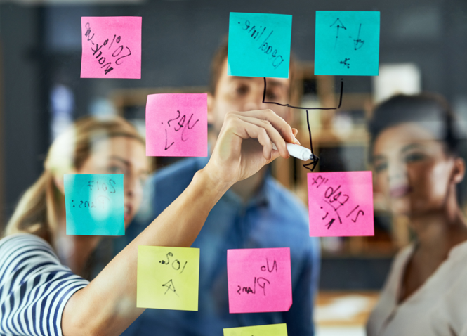 Group brainstorming with colorful sticky notes on glass board