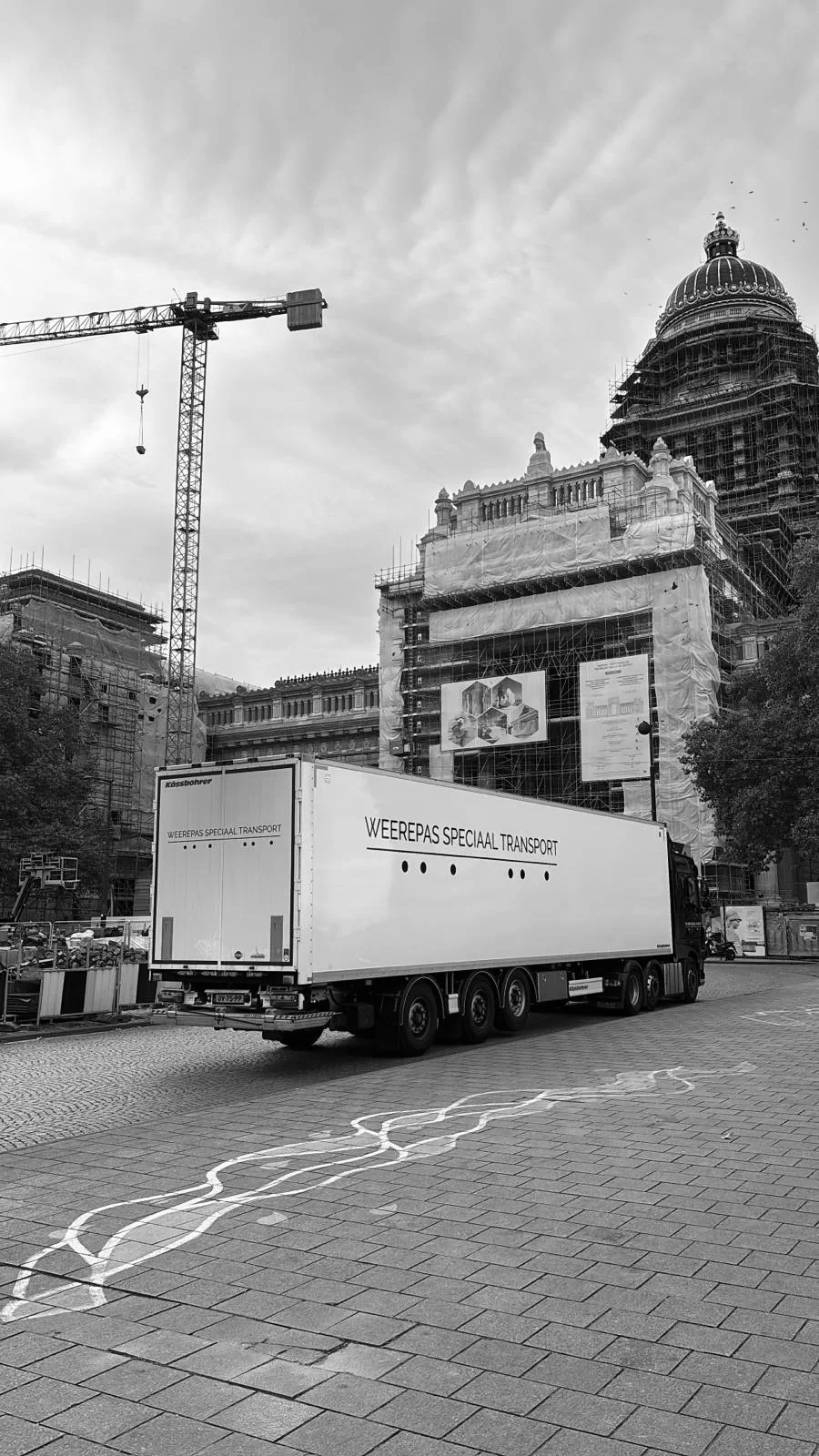 A delivery truck parked in front of a construction site with buildings under renovation, including a domed structure, in an urban area.