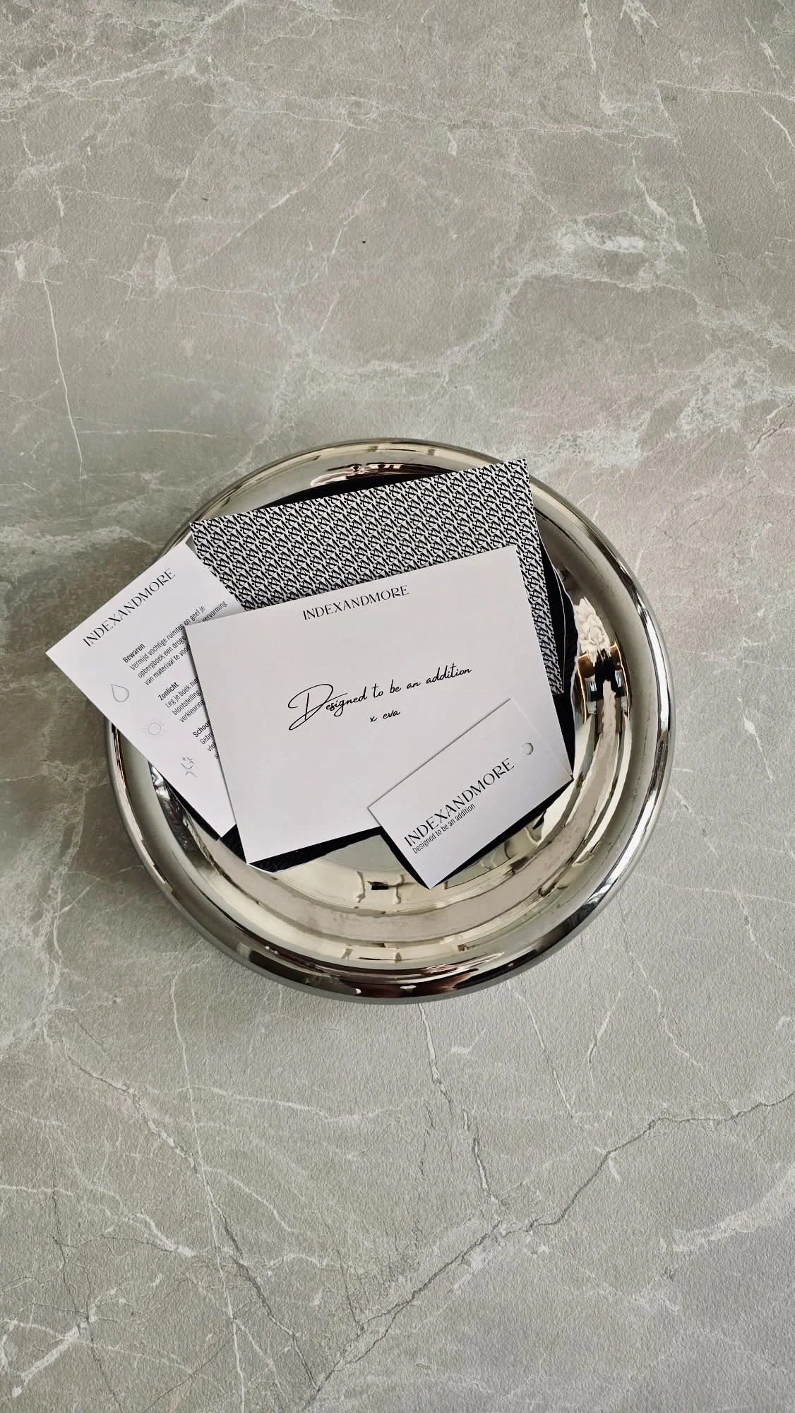 A silver circular tray holding various paper cards and a fabric sample on a light-colored marble surface.