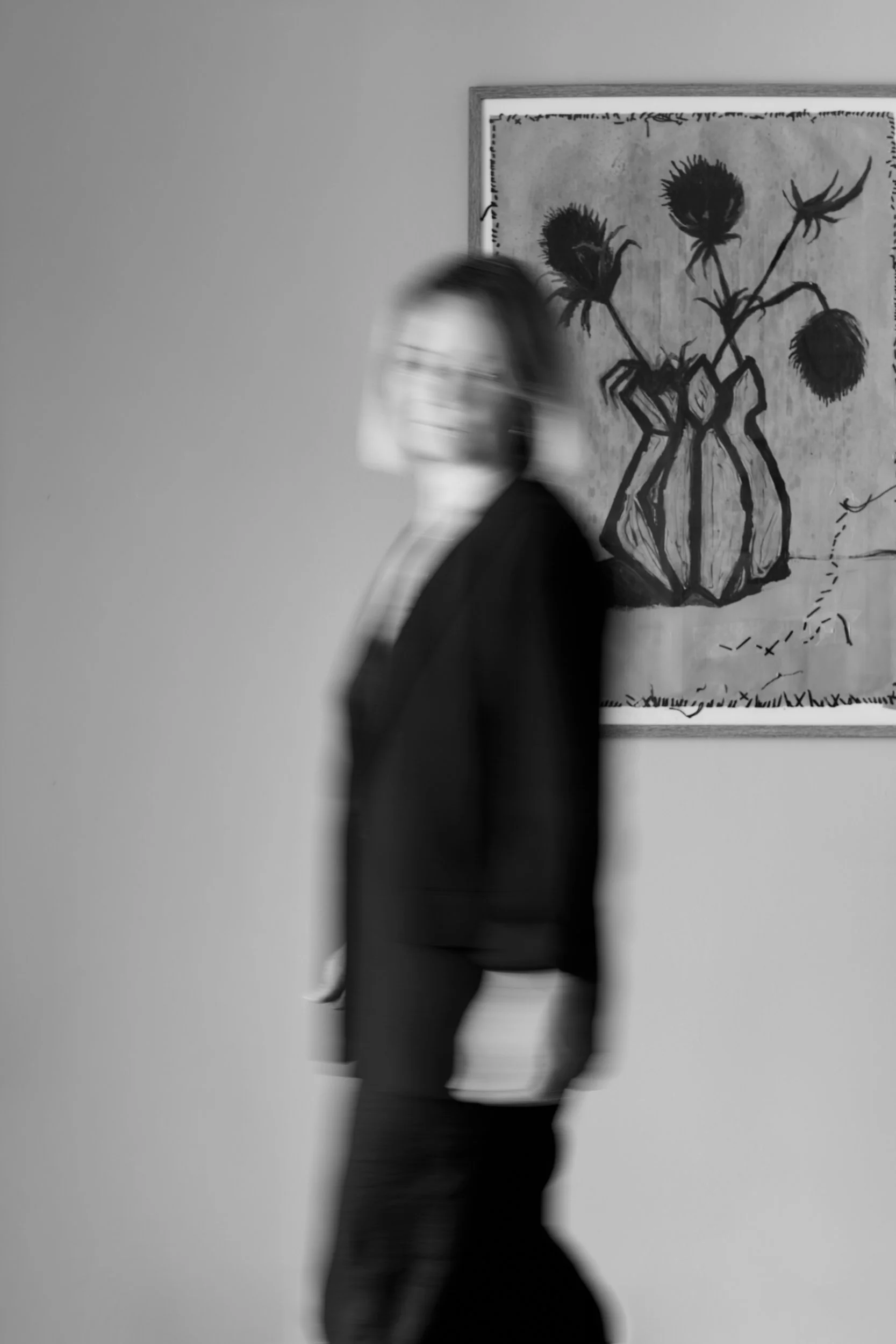 Sort/hvid foto af en person med maske, der går forbi en abstrakt kunstnerisk maleriet appelleret væg.