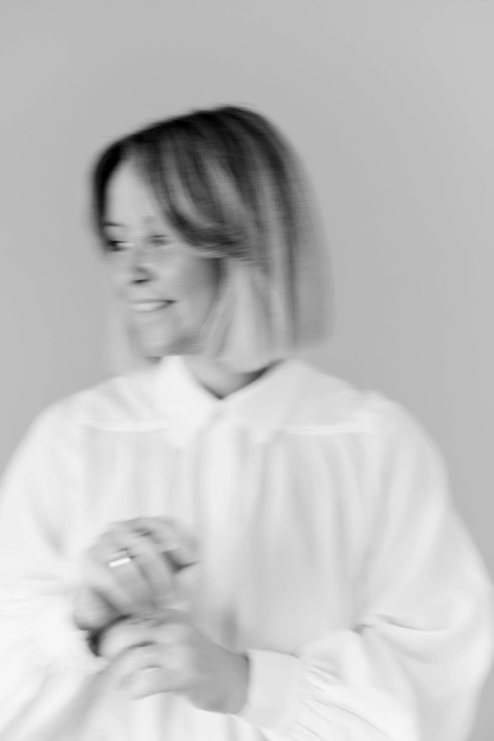 Sort-hvid portrætfoto af en kvinde med mørkt hår, der smiler, iført en hvid skjorte, med en neutral baggrund.