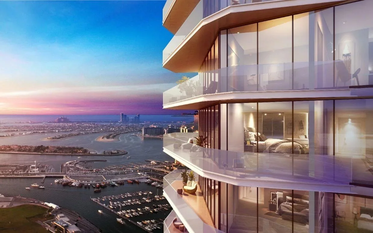 Modern high-rise building with glass balconies overlooking a marina and coastal cityscape during sunset.