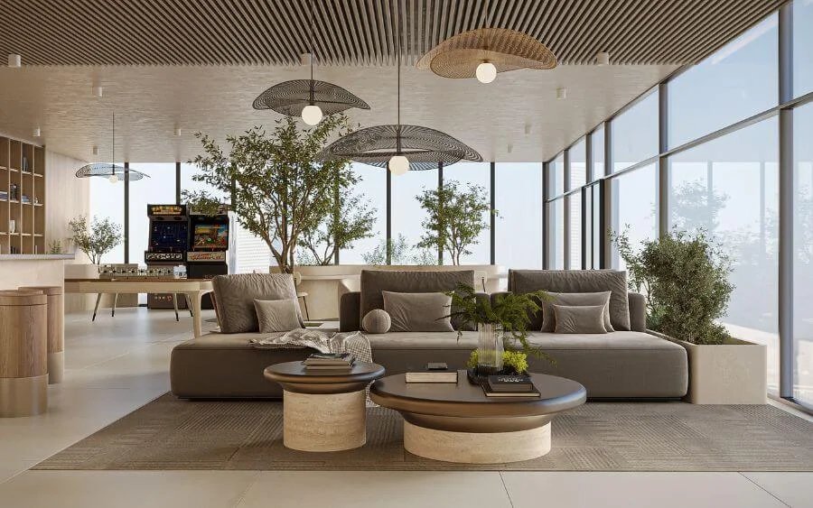 Modern lounge area with large gray sofa, round coffee tables, and indoor plants; arcade machine visible in background; floor-to-ceiling windows and wooden ceiling.
