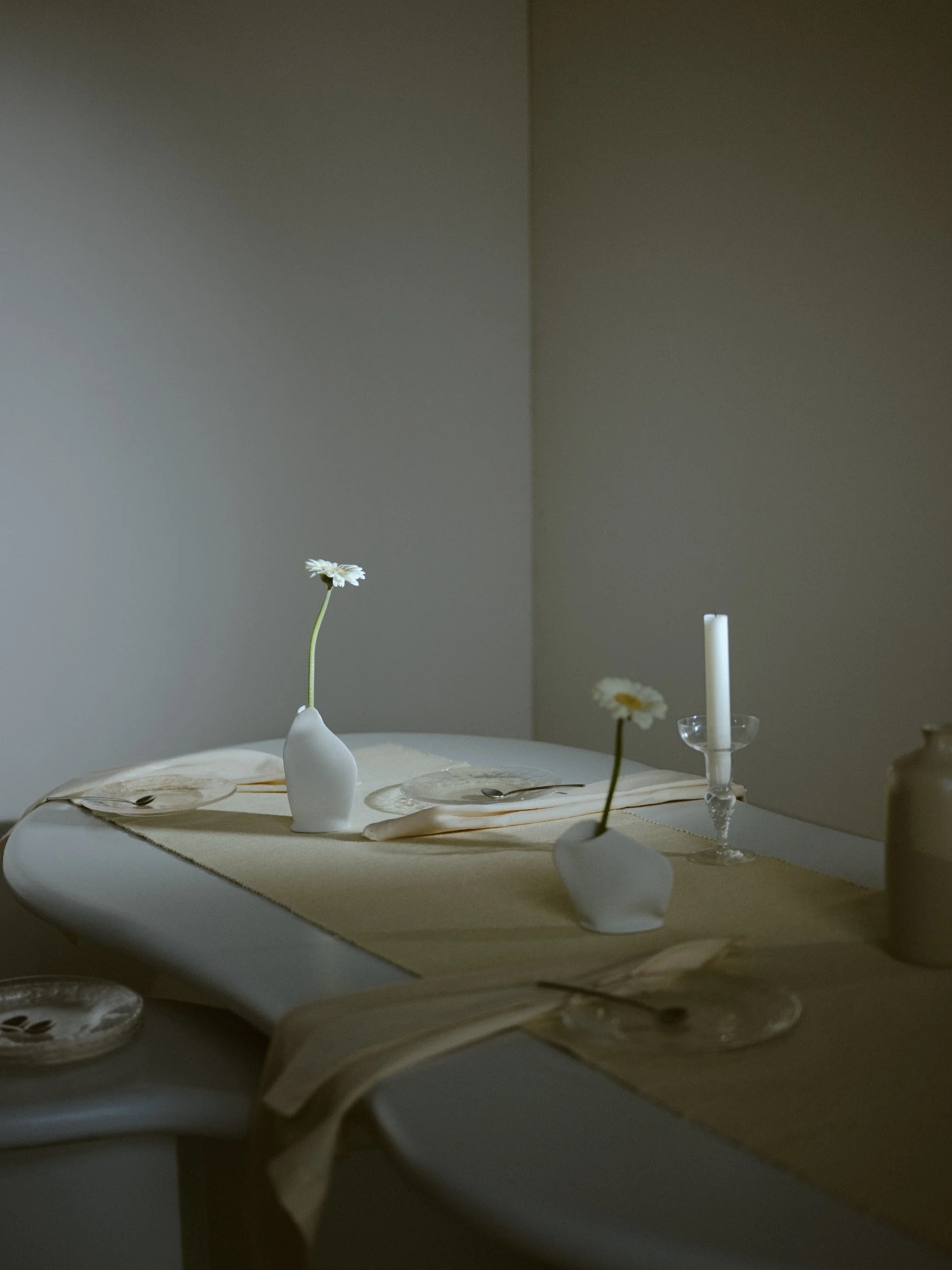 Minimalistisk dukning på ett bord med vita vaser med blommor, en levande ljus i en ljusstake och tallrikar med bestick.