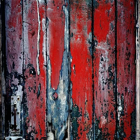 Close-up of a weathered wooden door with peeling red, blue, and black paint.