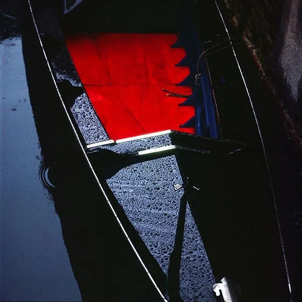 A black boat on calm water with a red and black canopy or cover inside the boat.