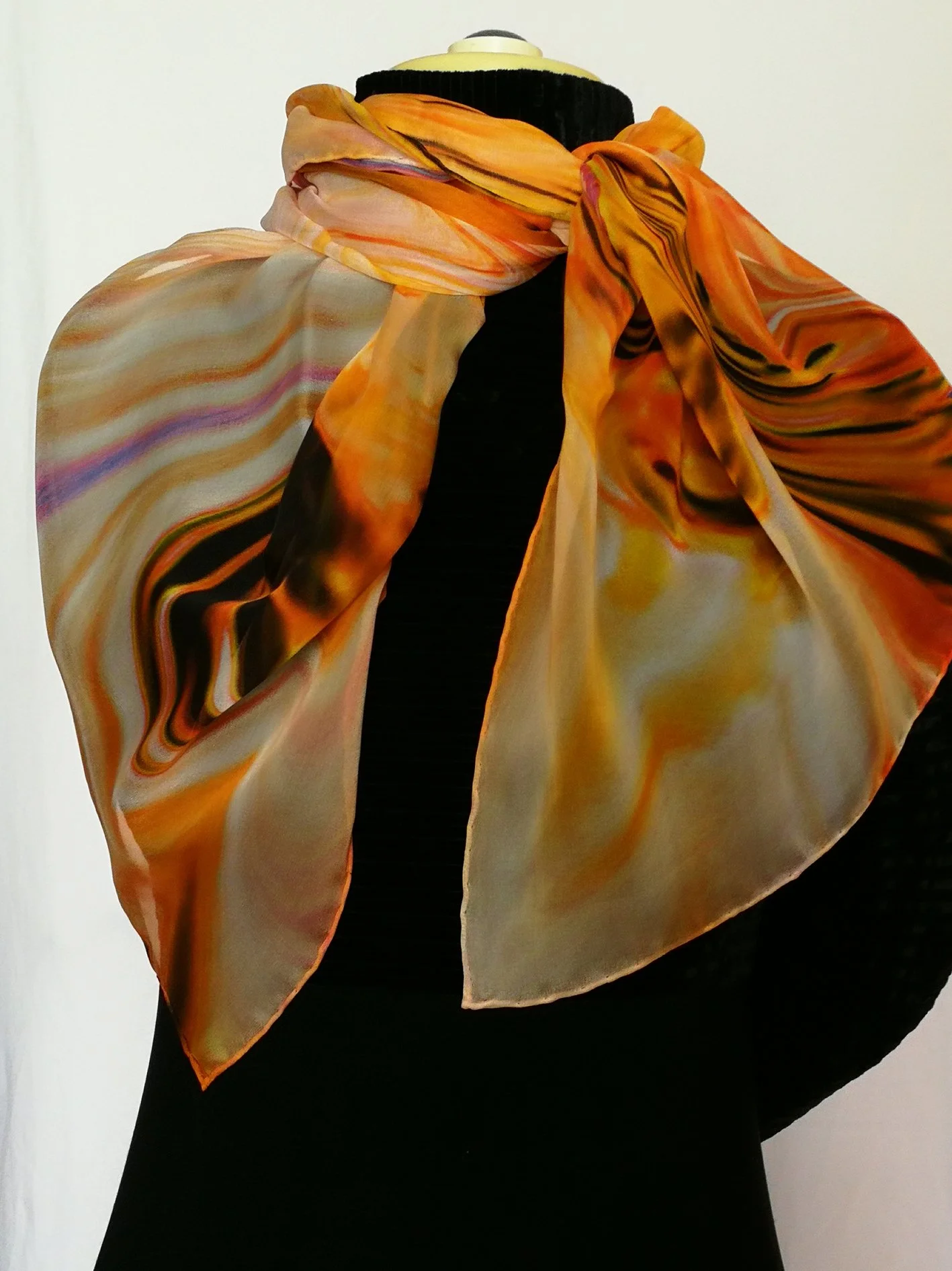 A mannequin wearing a vibrant, multicolored scarf with orange, yellow, and black swirls, draped over a black top, against a plain white background.