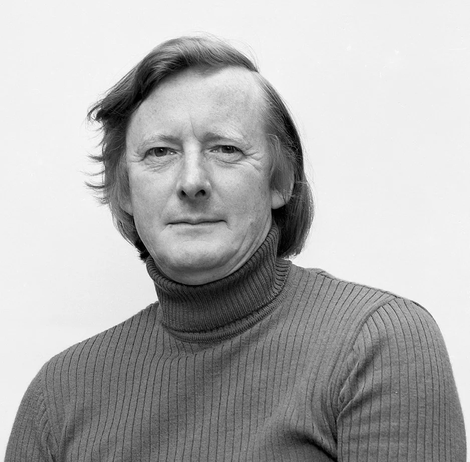 Black and white portrait of a man with shoulder-length hair, wearing a turtleneck sweater, looking at the camera with a slight smile.